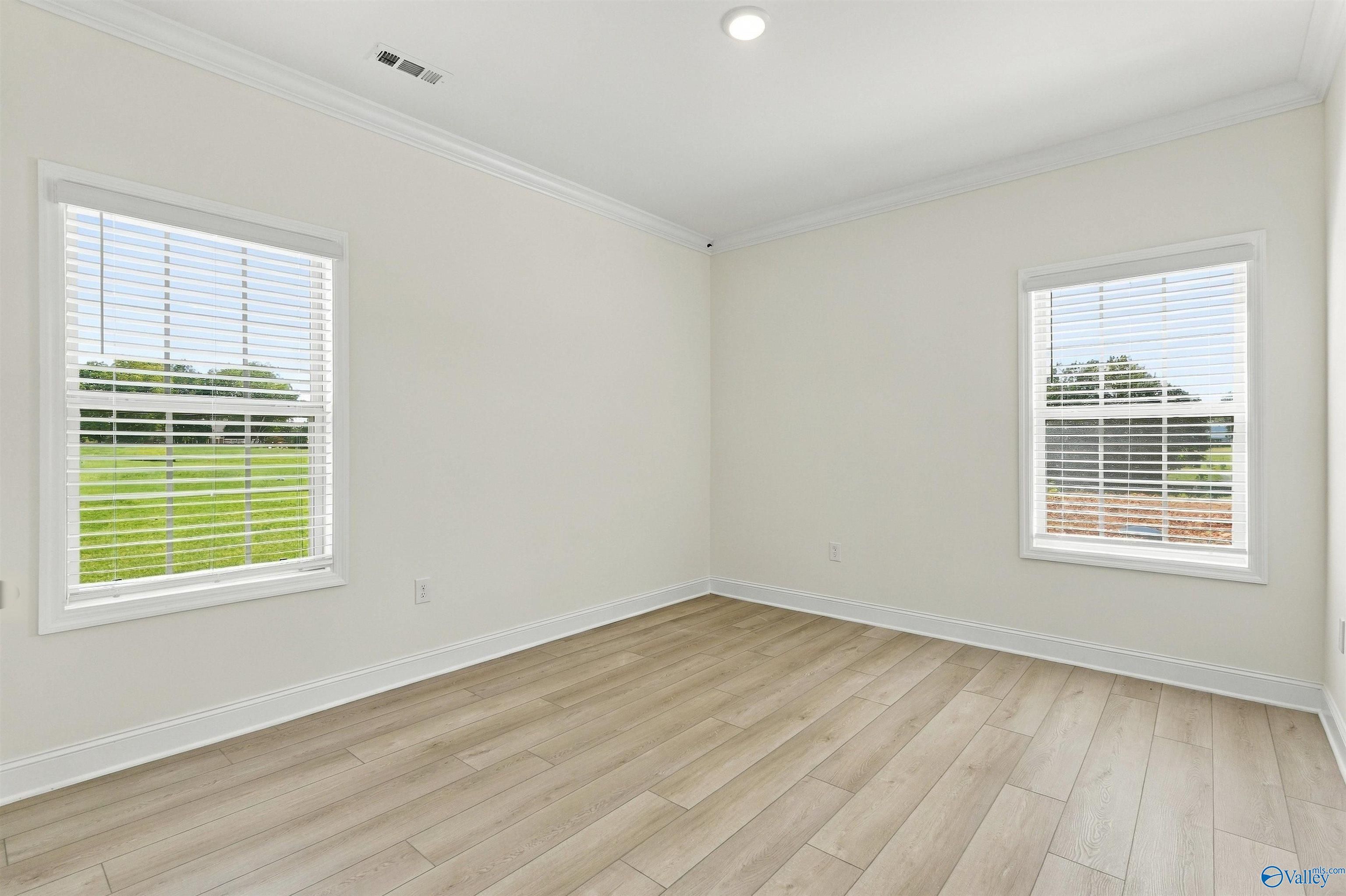 Bright bedroom with luxury vinyl plank flooring, crown molding, and two windows overlooking the yard in Davidson Homes' The Valencia, Huntsville, Alabama.