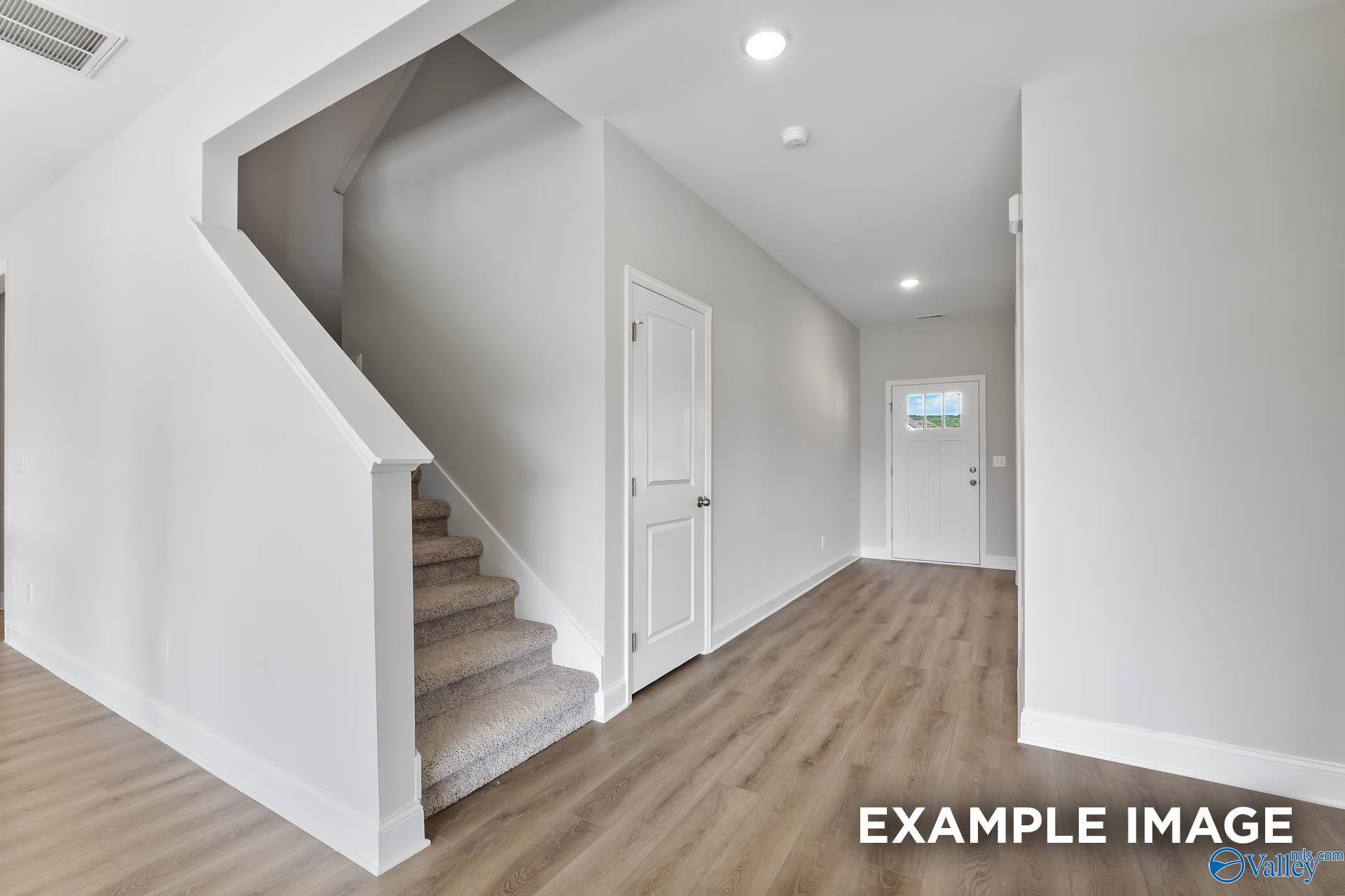 Bright foyer with luxury vinyl plank flooring, carpeted staircase, and front door in Davidson Homes Chelsea C, Hartselle, Alabama