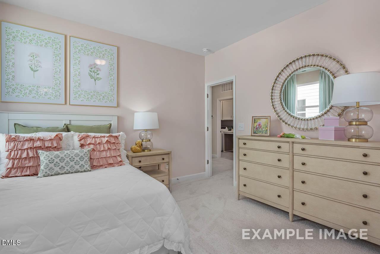Serene bedroom with soft pink walls, white bed, pink pillows, wooden dresser, gold mirror in Davidson Homes The Hickory II C, Wake Forest, NC