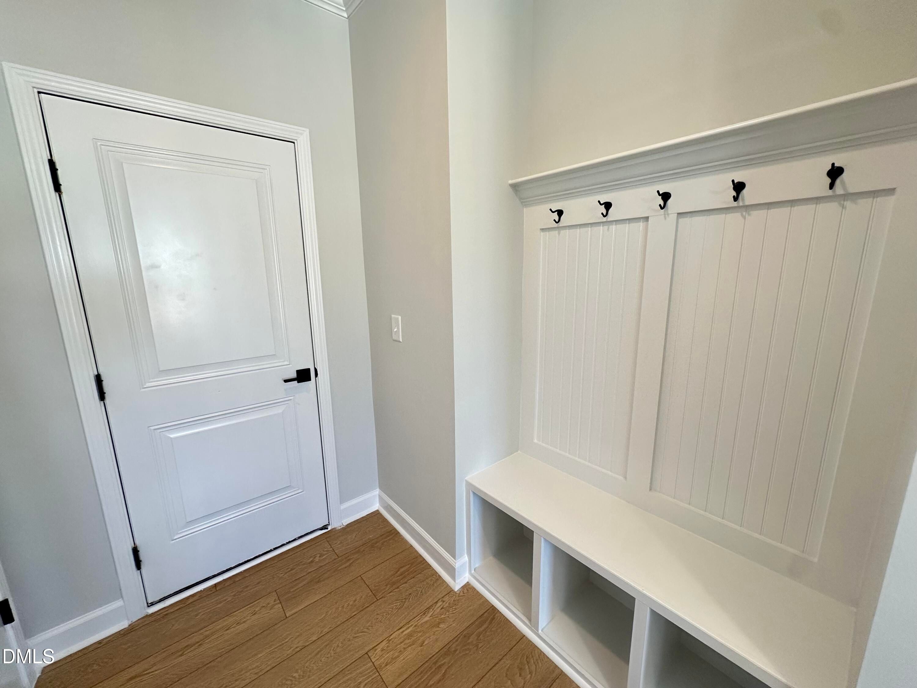 White mudroom with built-in bench, coat hooks, and storage cubbies beside paneled door in Davidson Homes The Avery, Knightdale, NC
