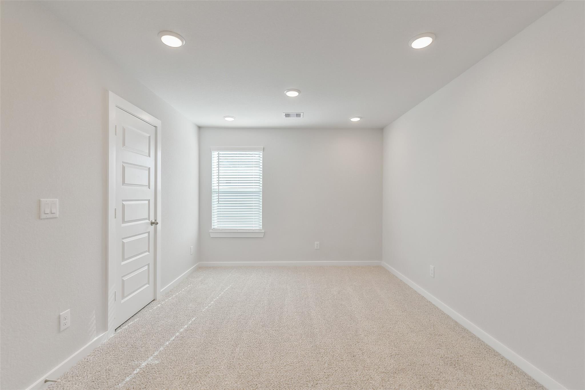 Spacious empty bedroom with beige carpet, neutral walls, paneled door, and window blinds in Davidson Homes The Trinity F, Magnolia, Texas