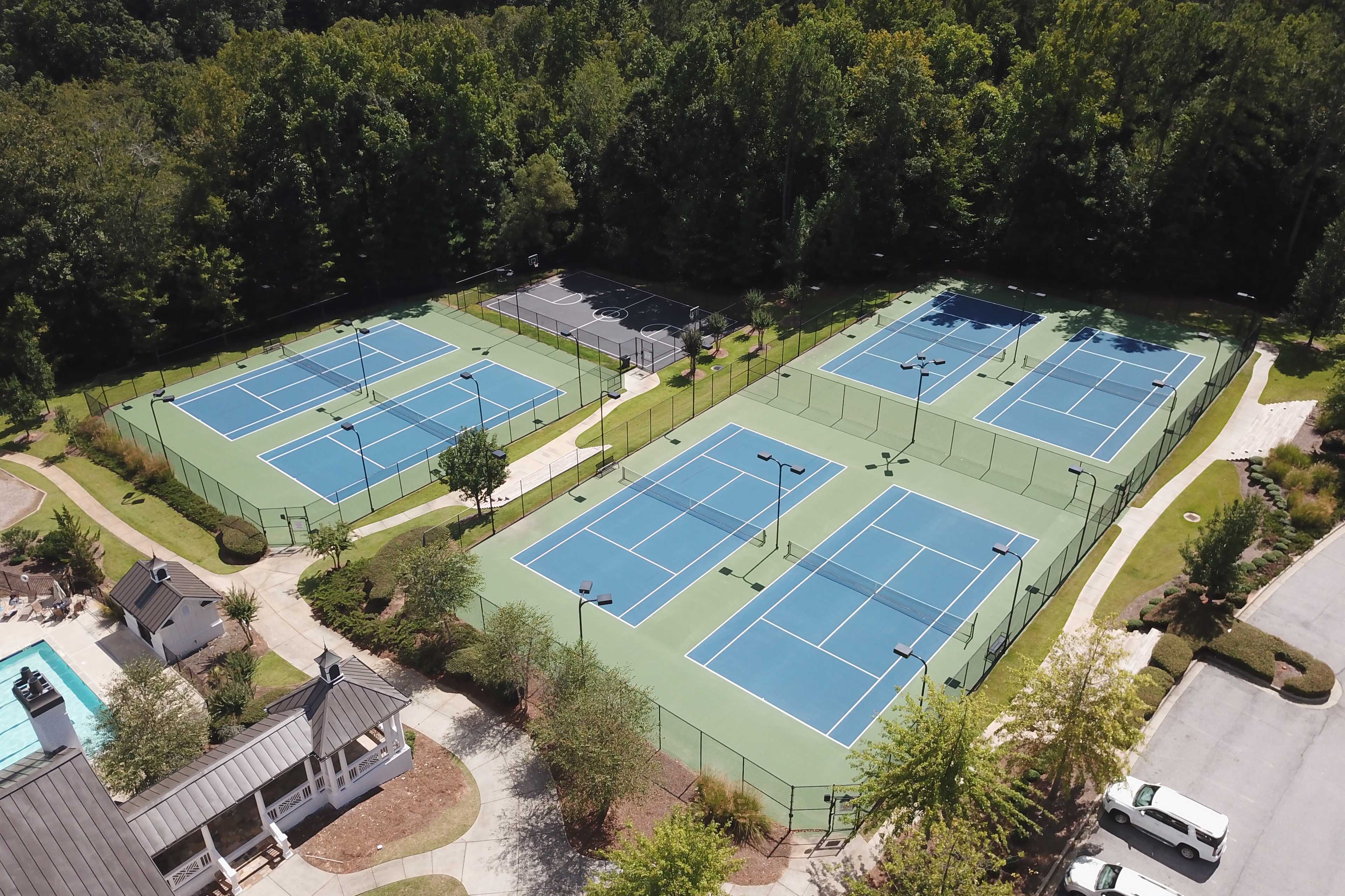 Aerial view of blue tennis courts and resort-style pool at Riverwood in Dallas Georgia by Davidson Homes with lush greenery