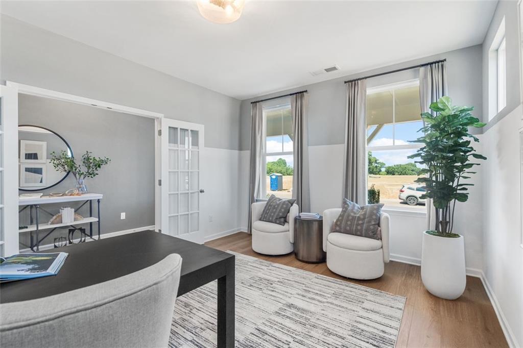 Cozy home office with wooden desk, armchairs, round mirror, and large windows in Davidson Homes The Hickory C, Hoschton, GA