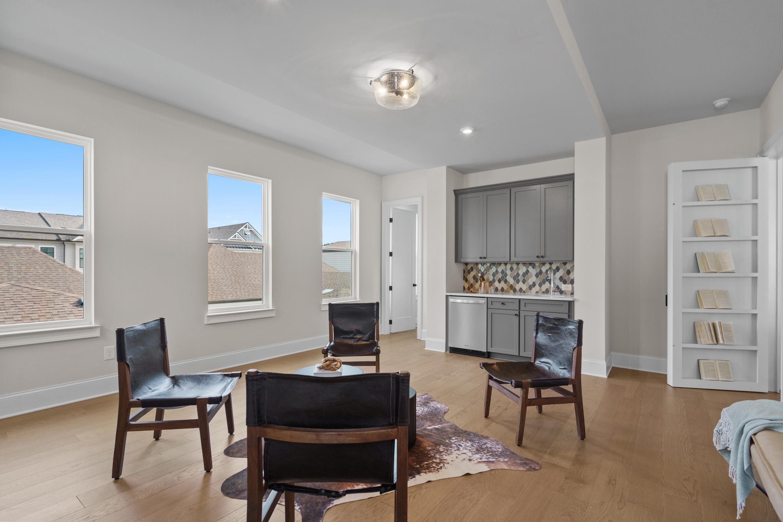 Spacious loft living area at The Village at Towne Lake in Woodstock GA with leather chairs, cowhide rug, hardwood floors, and gray bar cabinetry