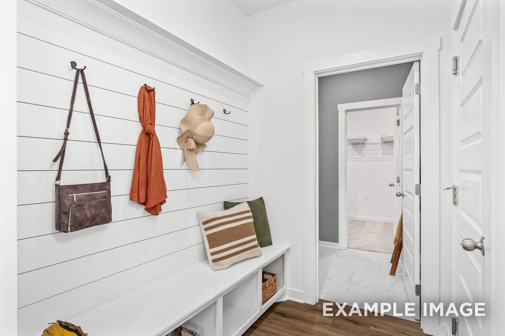 Organized mudroom with shiplap walls, hanging handbag, scarf, hat, cushioned bench, and laundry access in Davidson Homes The Ash A, Gallatin, TN