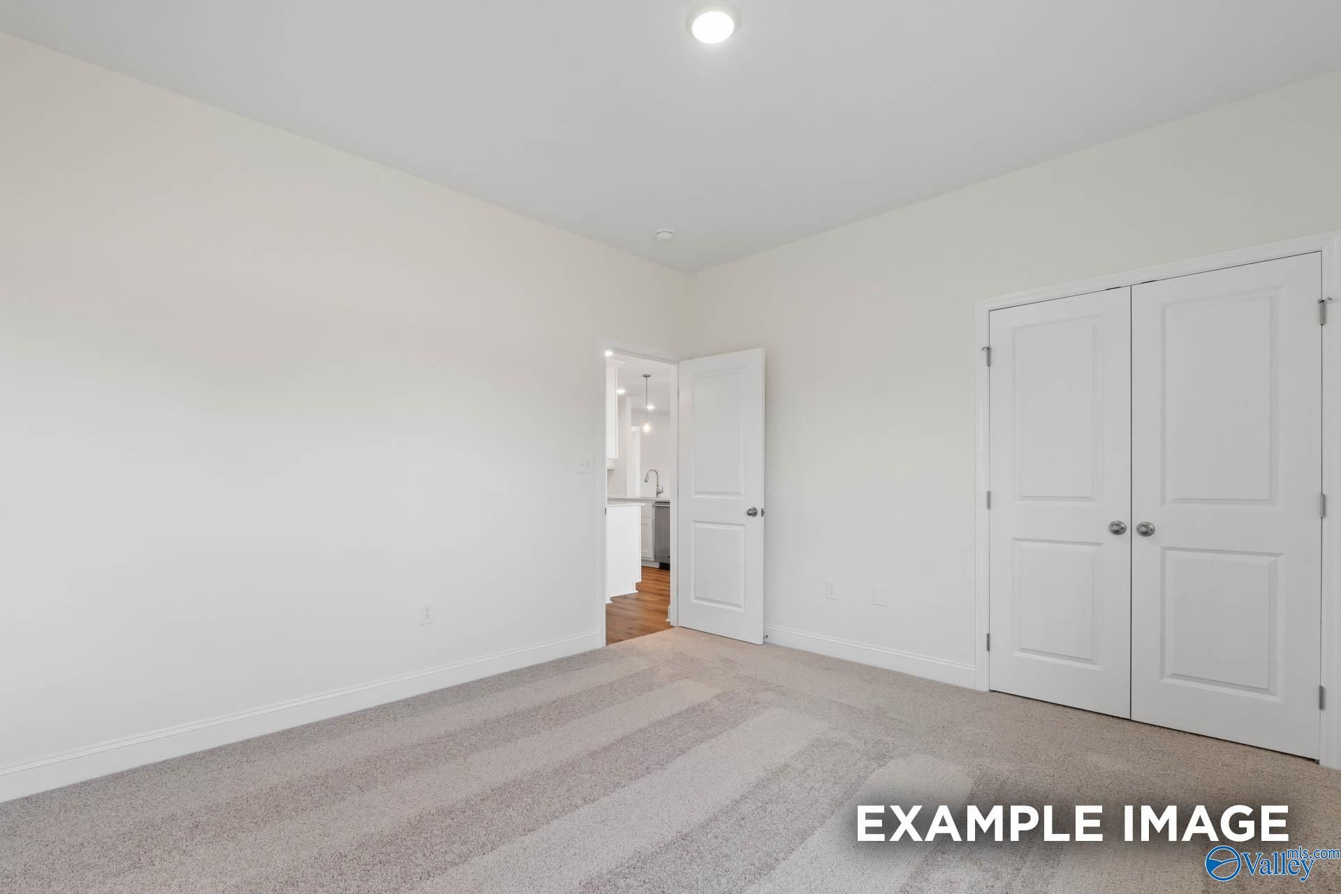 Spacious bedroom featuring neutral carpet, double closet doors, and open entry to adjacent room in Davidson Homes The Oxford, Huntsville AL