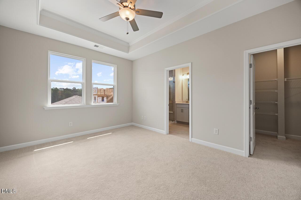 Primary bedroom with tray ceiling, ceiling fan, and walk-in closet in The Alexander C by Davidson Homes, Knightdale, NC.