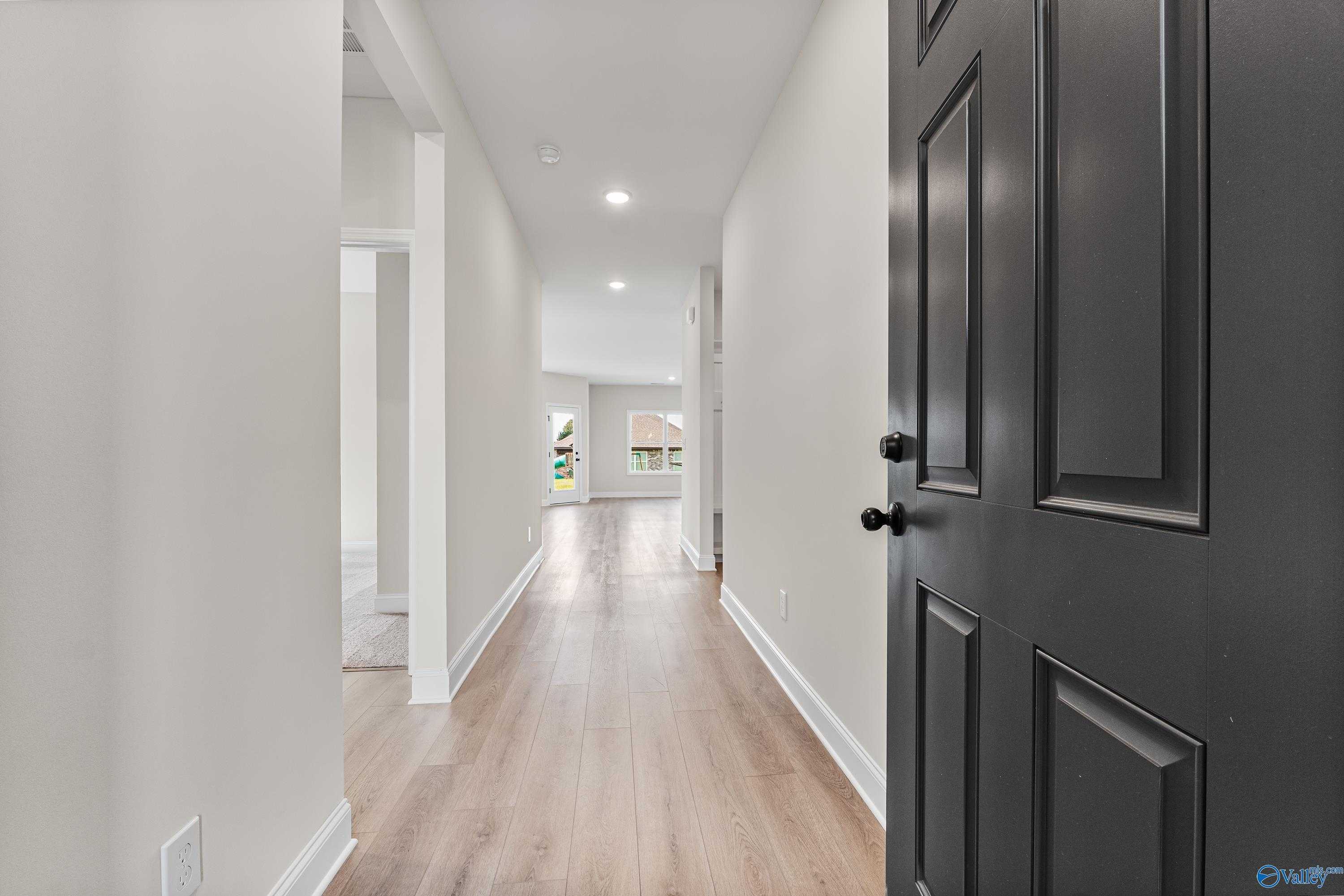 Bright hallway with light oak floors, neutral walls, and black door in Davidson Homes The Franklin B, Hazel Green, Alabama