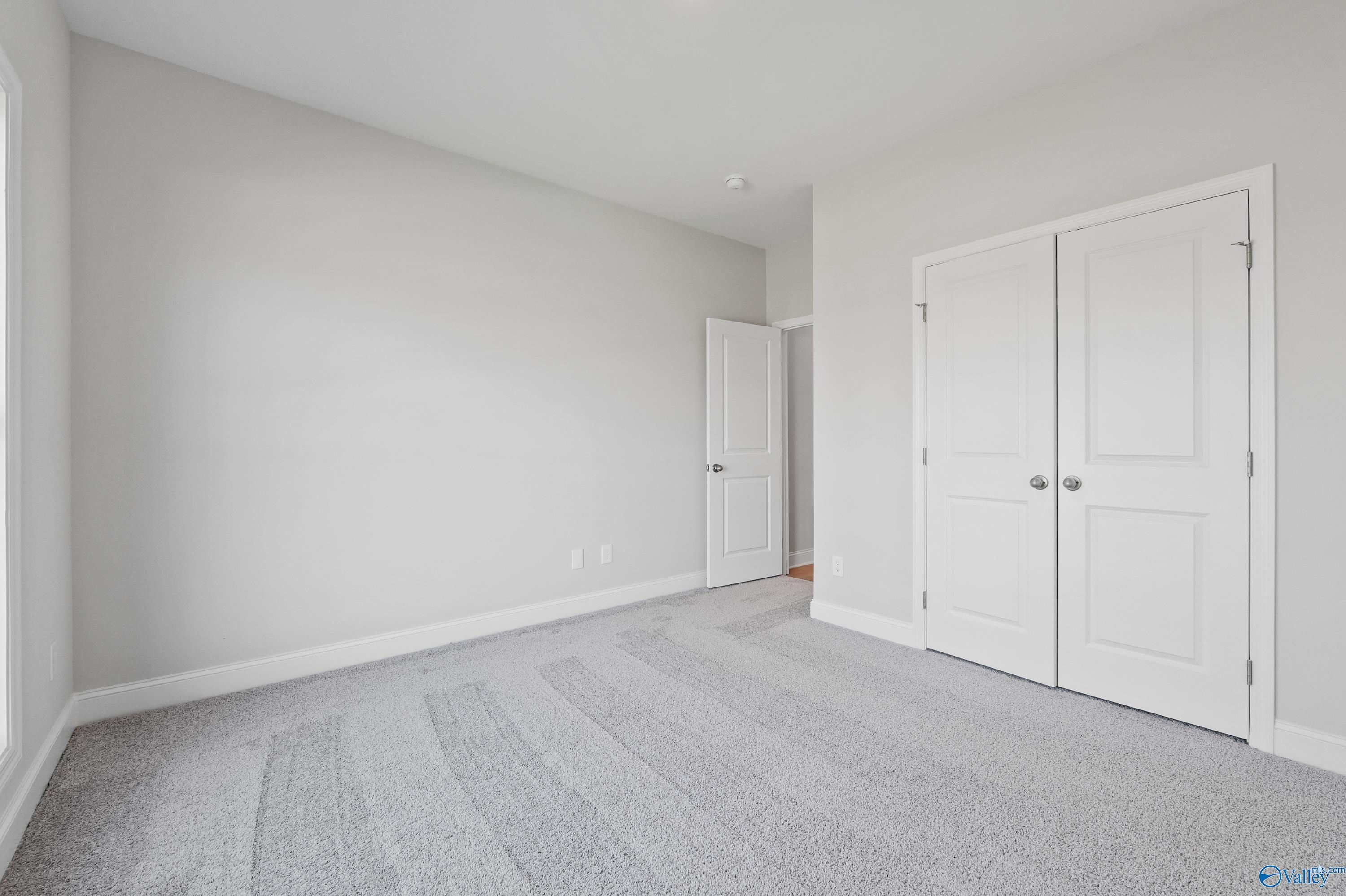 Bright secondary bedroom with gray walls, white double closet doors, and carpet floor in Davidson Homes The Everett, Hazel Green, AL