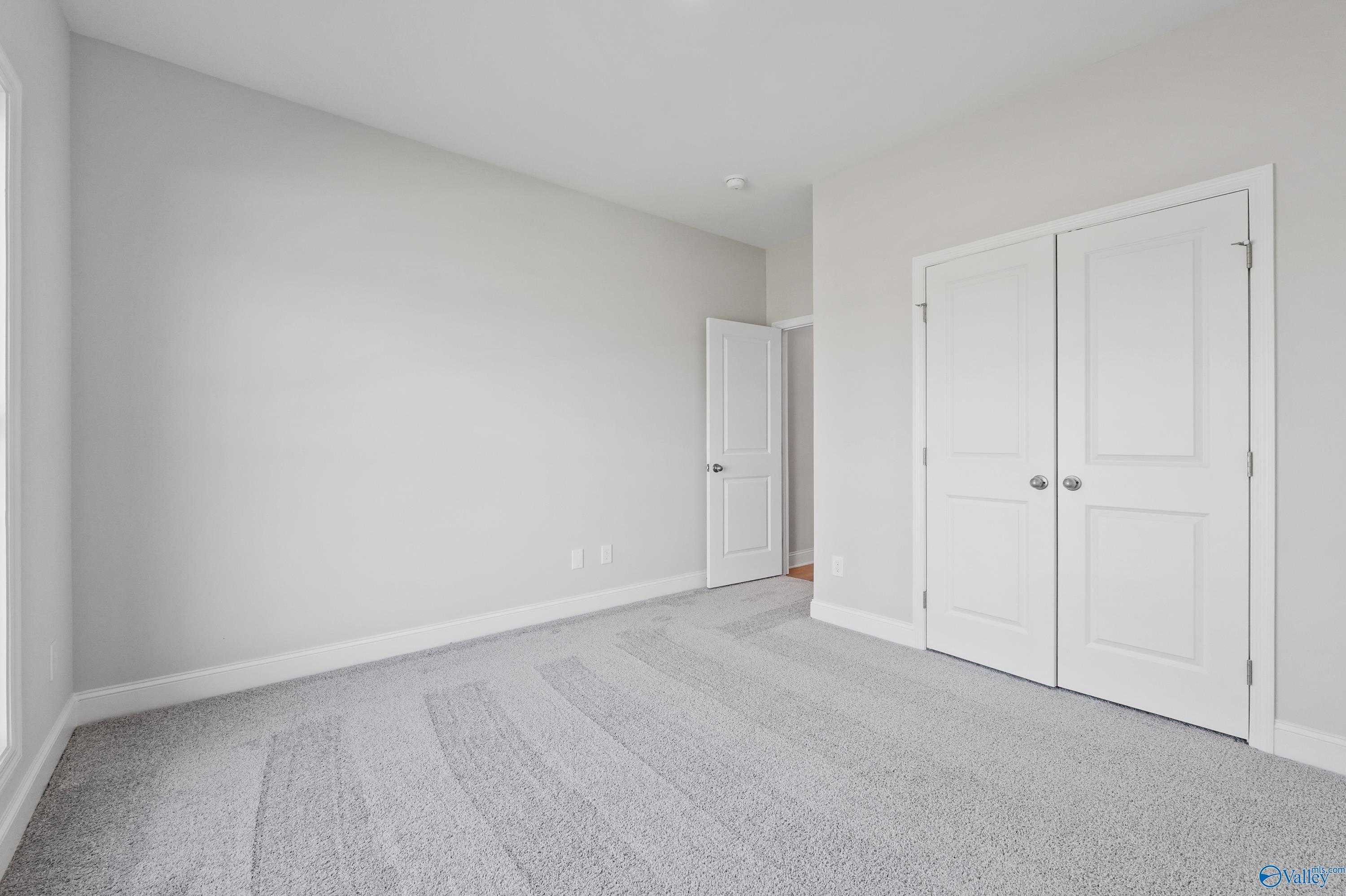 Bright secondary bedroom with gray walls, white double closet doors, and carpet floor in Davidson Homes The Everett, Hazel Green, AL