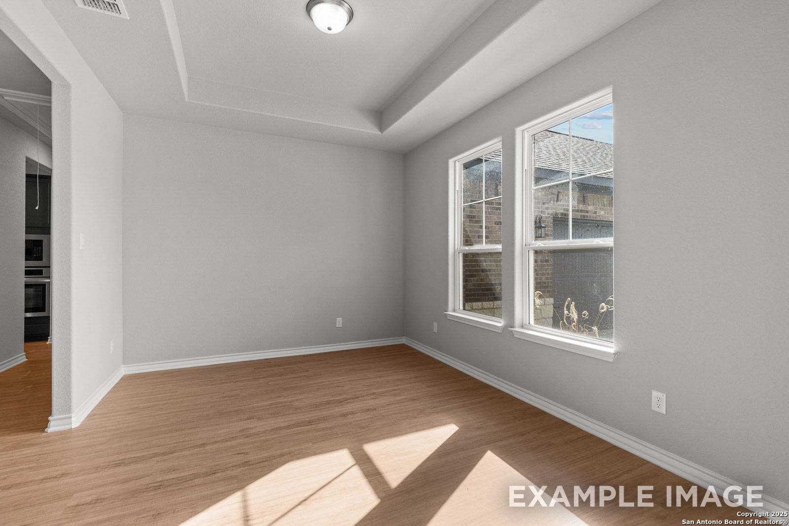 Bright dining area with tray ceiling and wood-style flooring in The Oxford F model by Davidson Homes in Castroville.