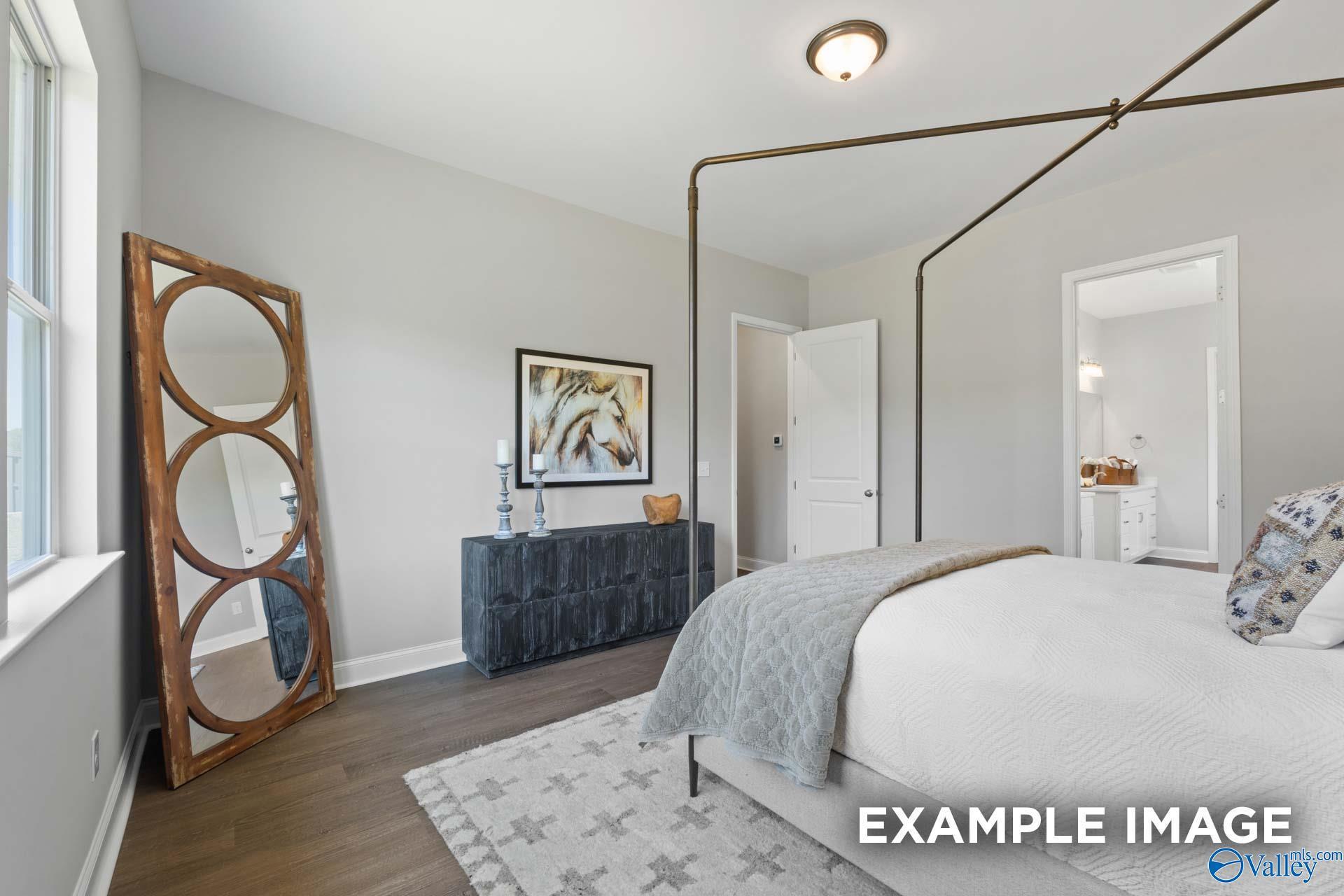 Elegant bedroom with king bed, arched wooden mirror, horse artwork, and en-suite door in Evermore Homes The Haven E, Owens Cross Roads, AL