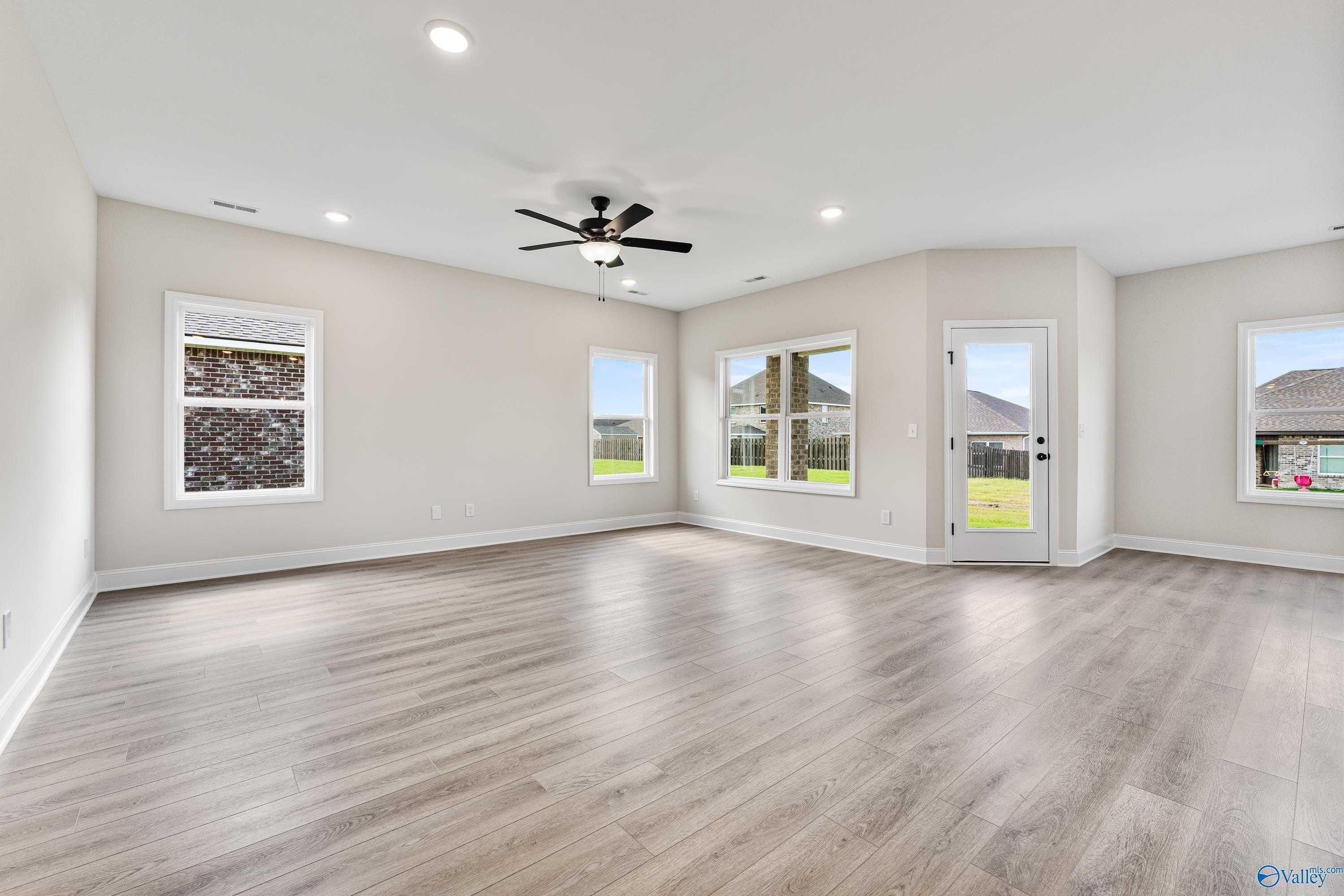 Spacious empty living room with beige walls, ceiling fan, large windows, and laminate flooring in Davidson Homes The Franklin B, Hazel Green, AL