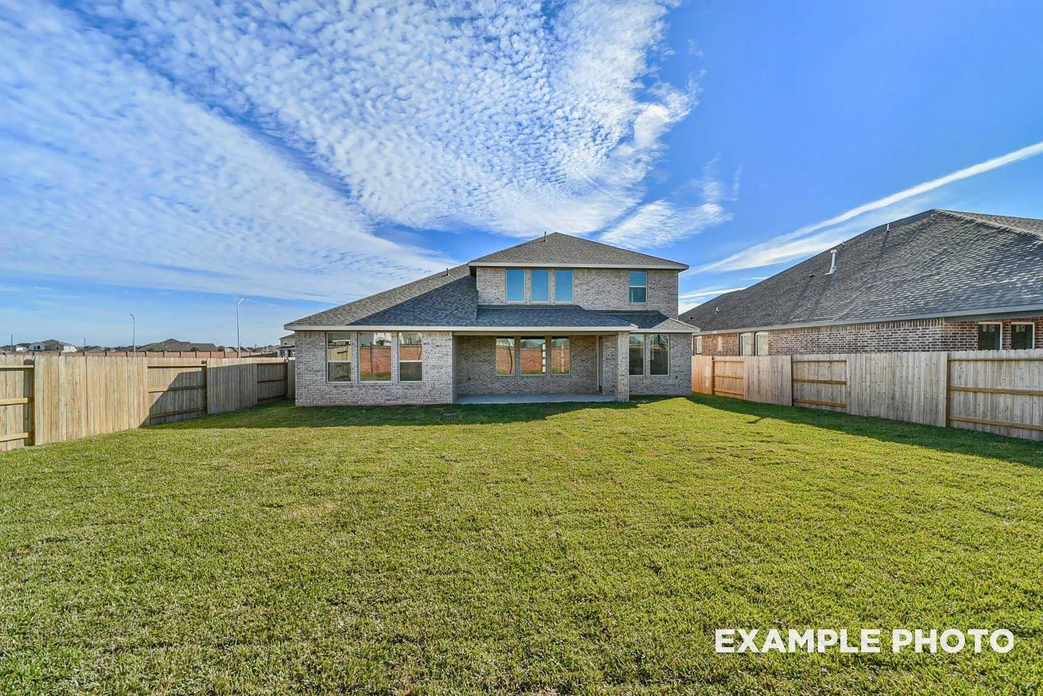 Rear view of one-story brick home with covered patio, lush green lawn, and wooden fence in Sierra Vista, Rosharon, Texas