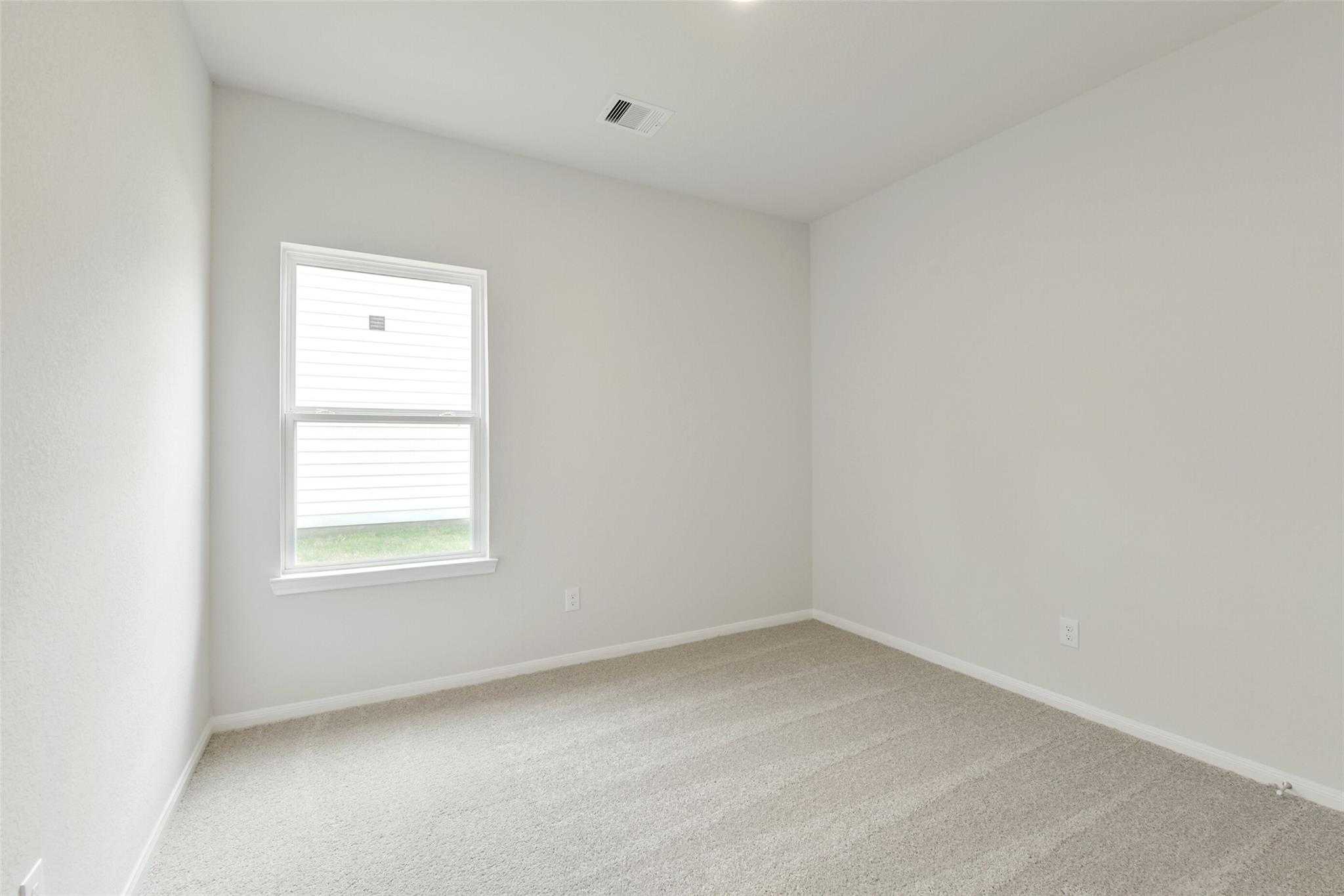 Bright secondary bedroom with beige carpet, white walls, and large window in Davidson Homes The Frio G, Conroe, Texas