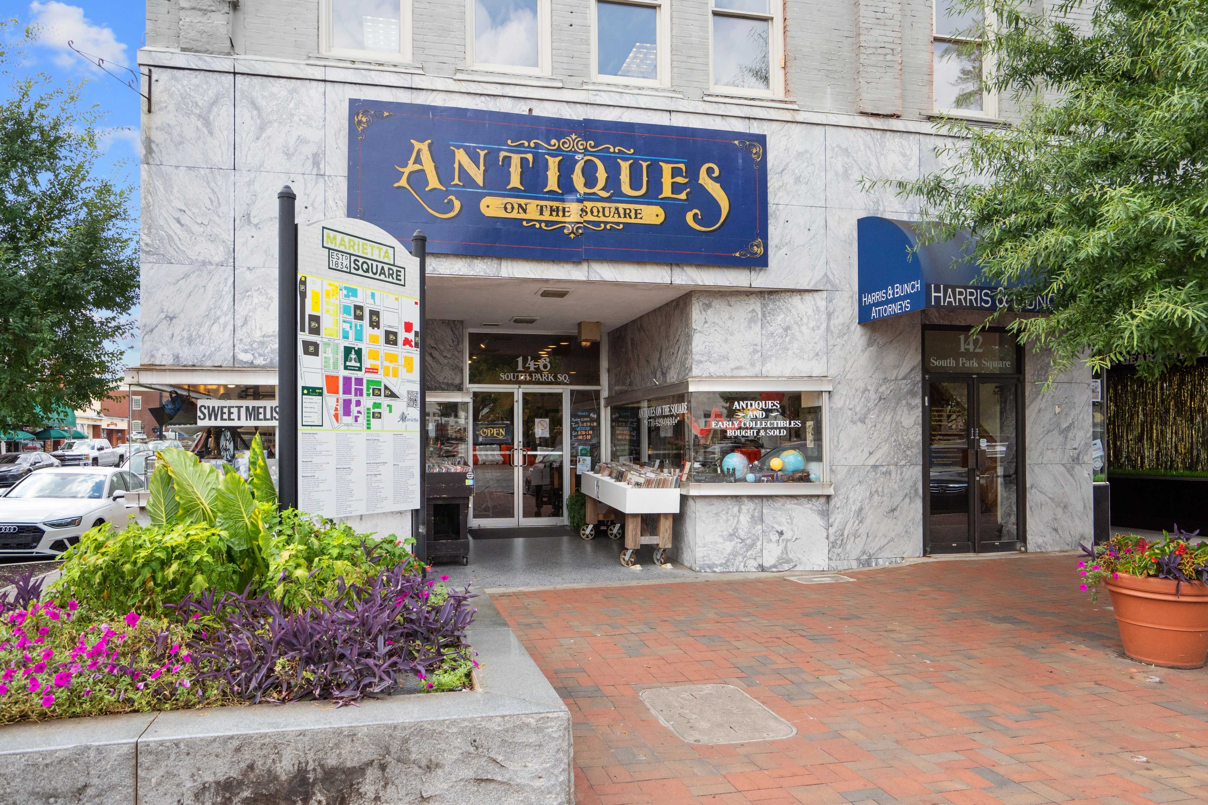 Charming antiques shop facade on Marietta Georgia square near Rosehill Townhomes with blue sign, brick sidewalk, potted plants and trees