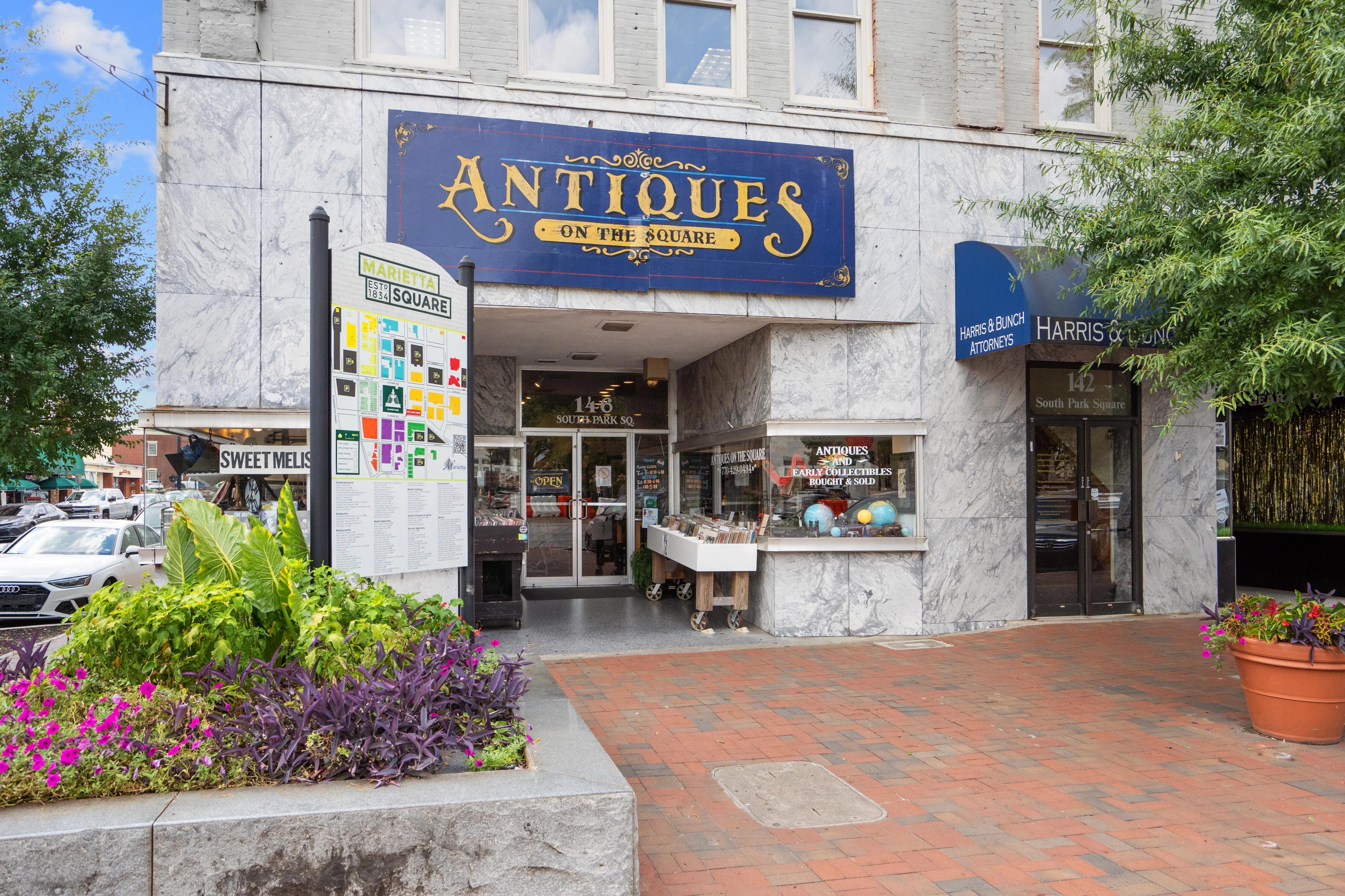 Charming antiques shop facade on Marietta Georgia square near Rosehill Townhomes with blue sign, brick sidewalk, potted plants and trees