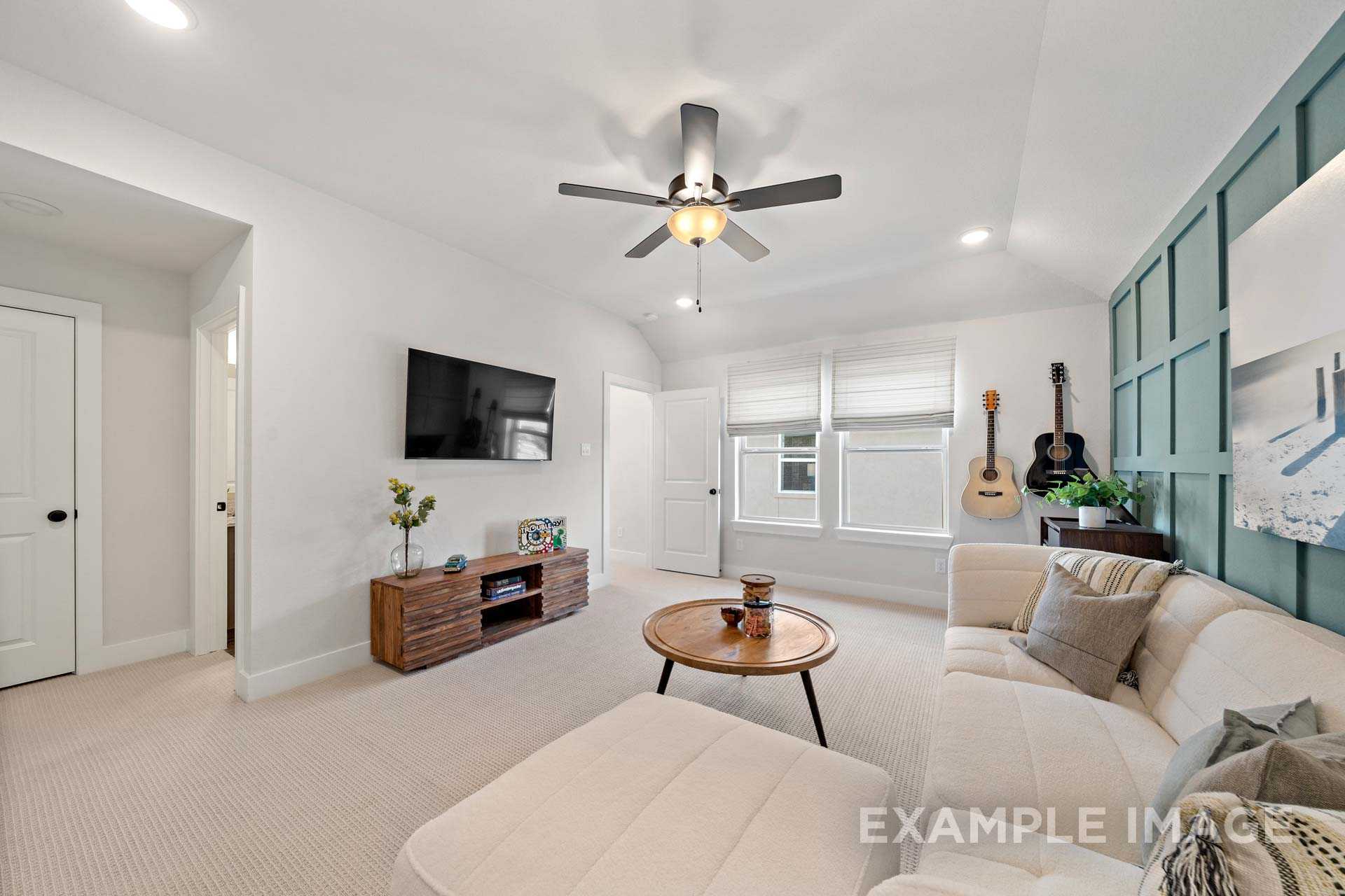 Spacious living room in The Edward B by Davidson Homes featuring beige sofa, wooden TV stand, ceiling fan, teal shiplap accent wall, and guitar decor
