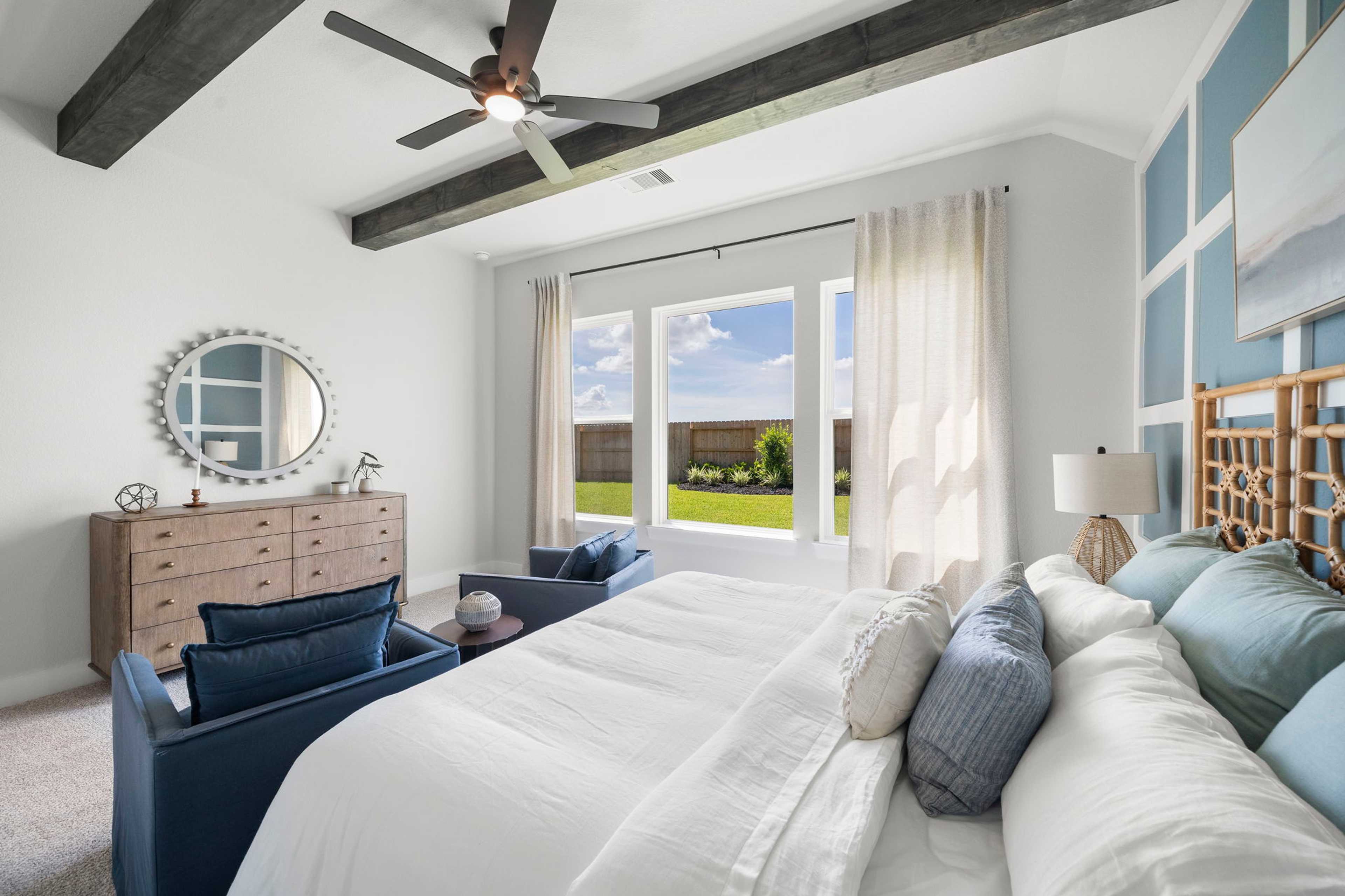 Coastal master bedroom in Lago Mar, Texas City TX by Davidson Homes with rattan headboard, white bedding, blue accents, and backyard view