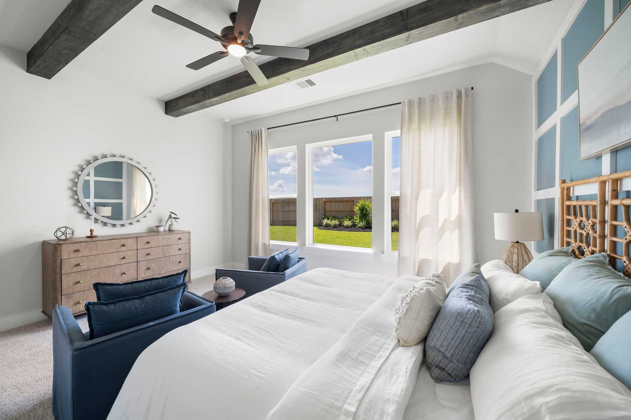 Coastal master bedroom in Lago Mar, Texas City TX by Davidson Homes with rattan headboard, white bedding, blue accents, and backyard view
