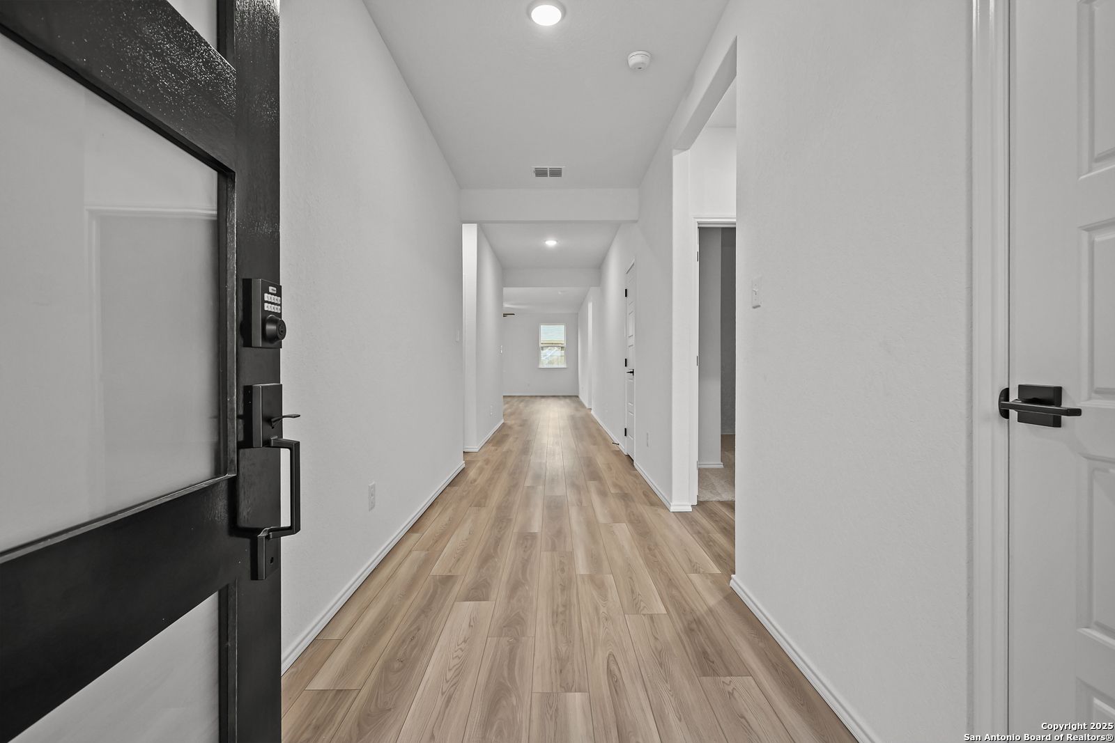 Bright hallway with light wood flooring, white walls, and open black door in Davidson Homes The Daphne J, Converse, Texas