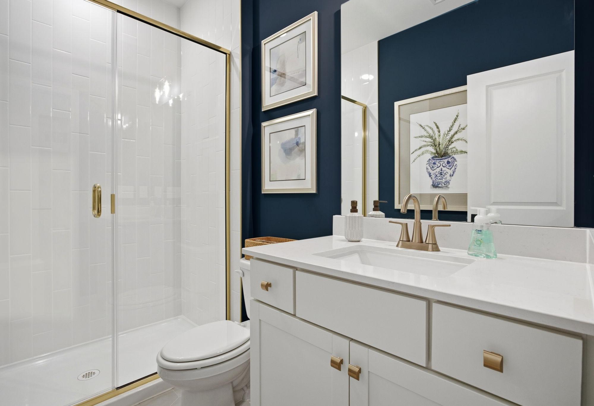 Modern bathroom in The Ashport featuring a walk-in glass shower, navy accent wall, and white vanity with gold hardware.