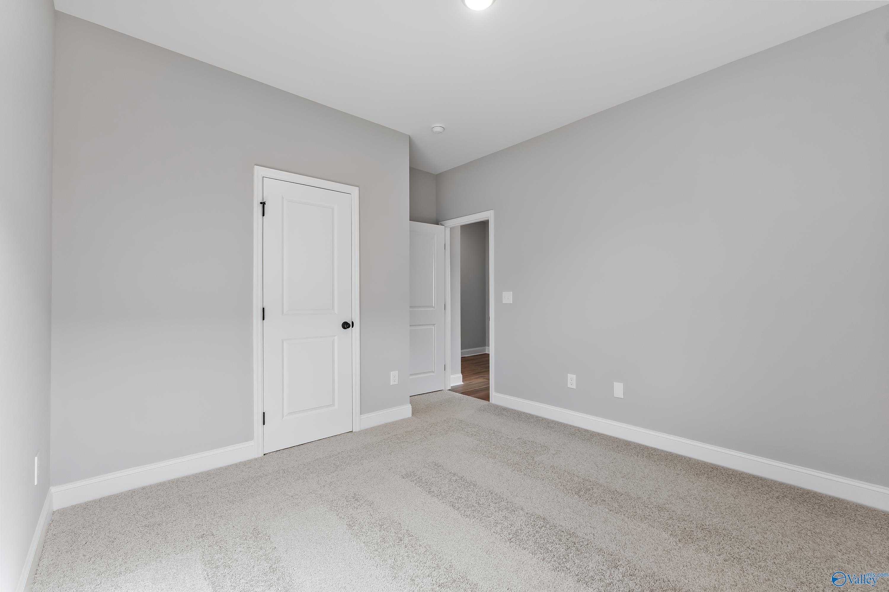 Empty bedroom with light gray walls, white doors, and neutral carpet in Davidson Homes The Franklin B, Hazel Green, Alabama