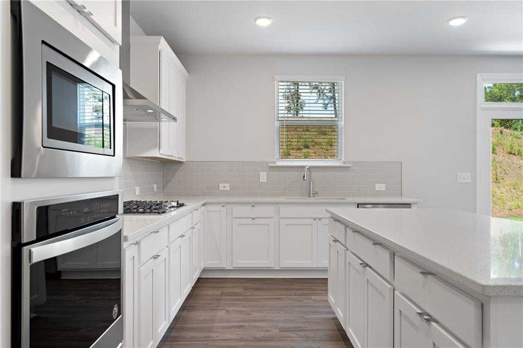Modern white shaker kitchen with stainless steel appliances, quartz island, and window view in Davidson Homes The Hickory B, Winder, GA