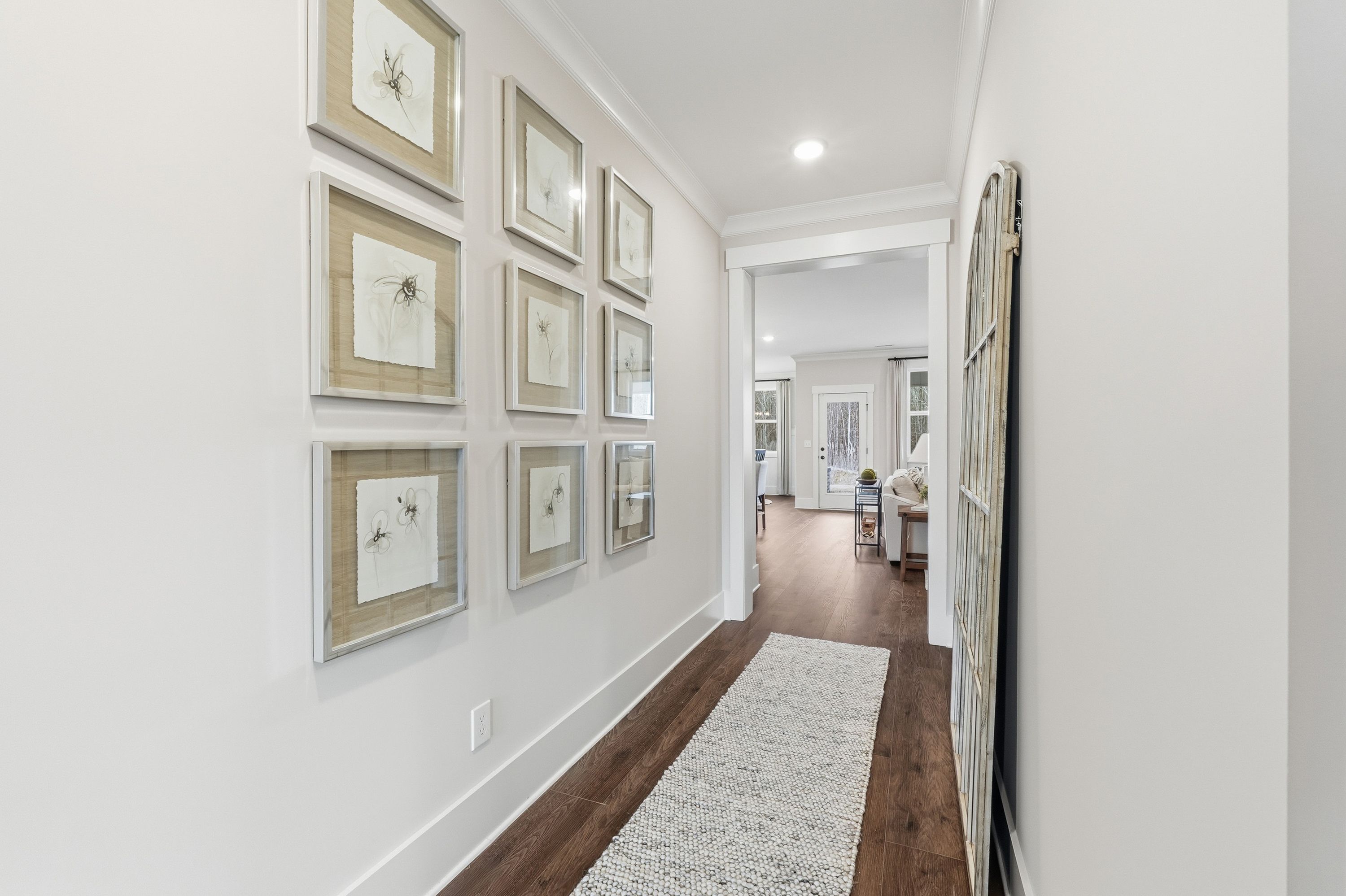 Spacious hallway in Noble Ridge Cullman AL home by Davidson Homes with hardwood floors white walls botanical art and barn door