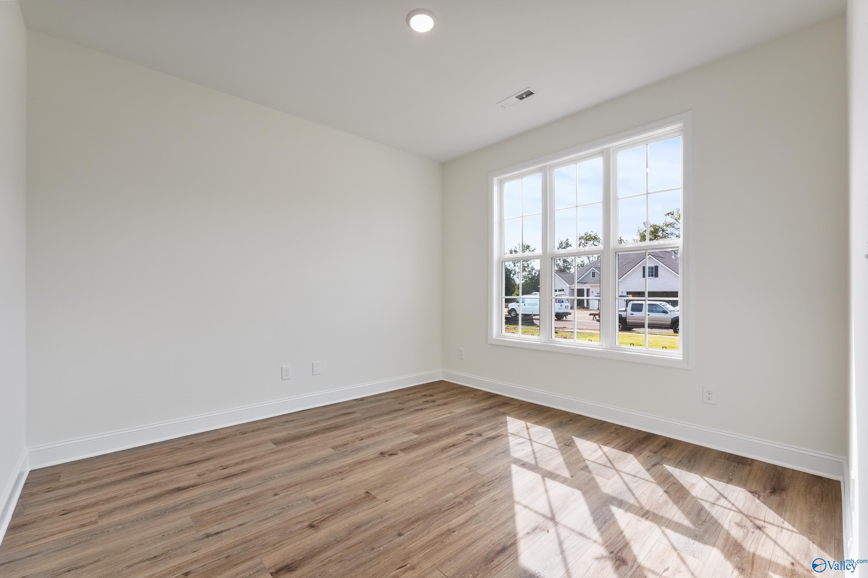 Bright empty bedroom with large triple windows and hardwood floors in Davidson Homes The Finleigh, Harvest, Alabama