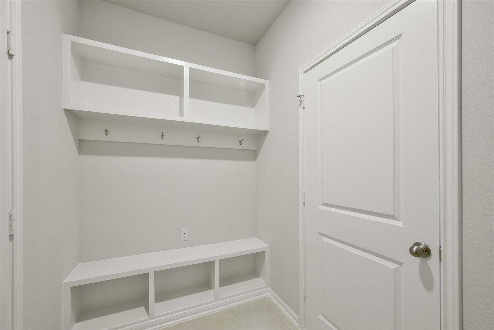 Functional mudroom with white open shelves, coat hooks, and storage bench in Davidson Homes The Sabine E, Dayton Texas