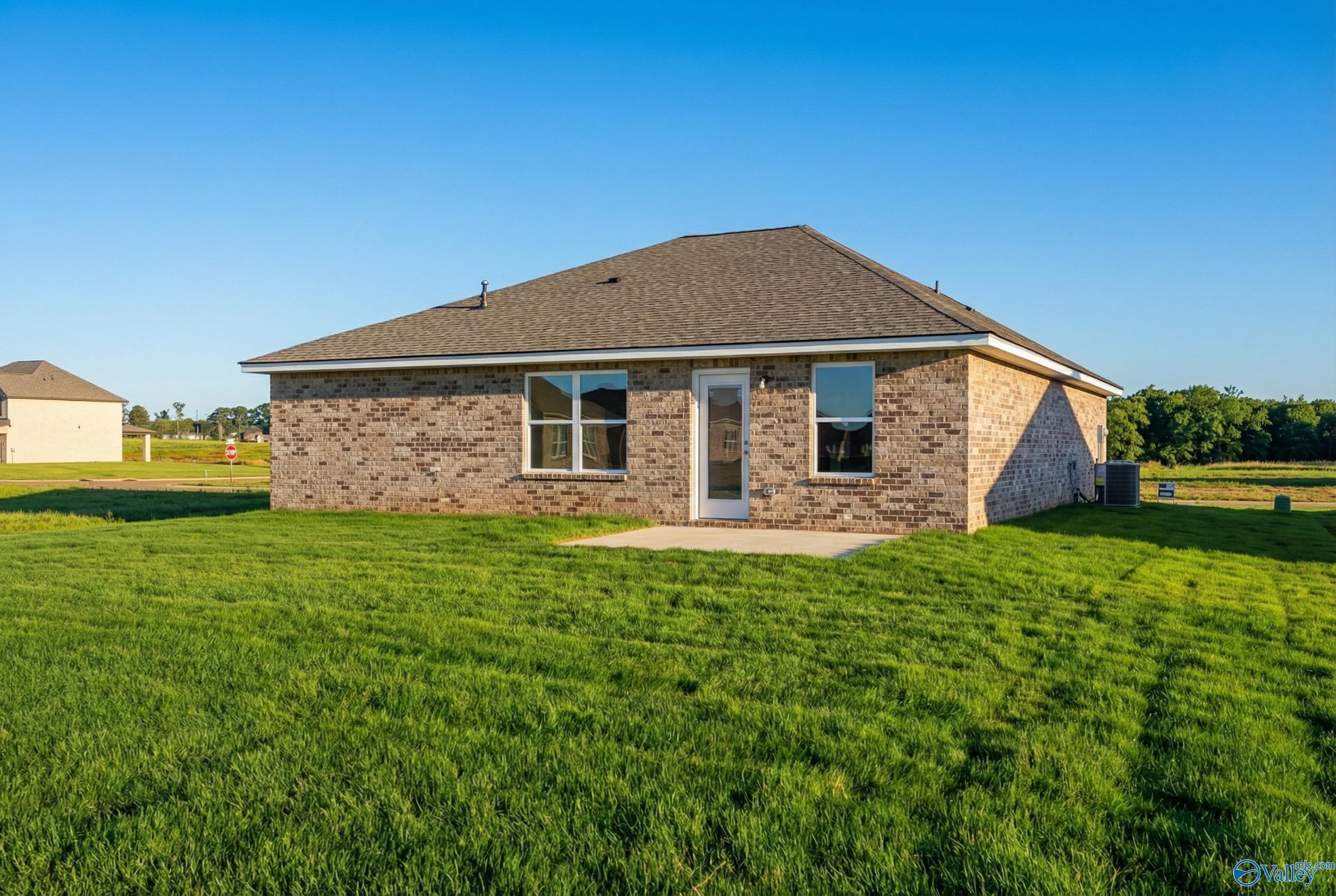 Covered back patio with brick exterior and lush green backyard in The Butler 3-bedroom home, Heritage Lakes, New Market, Alabama