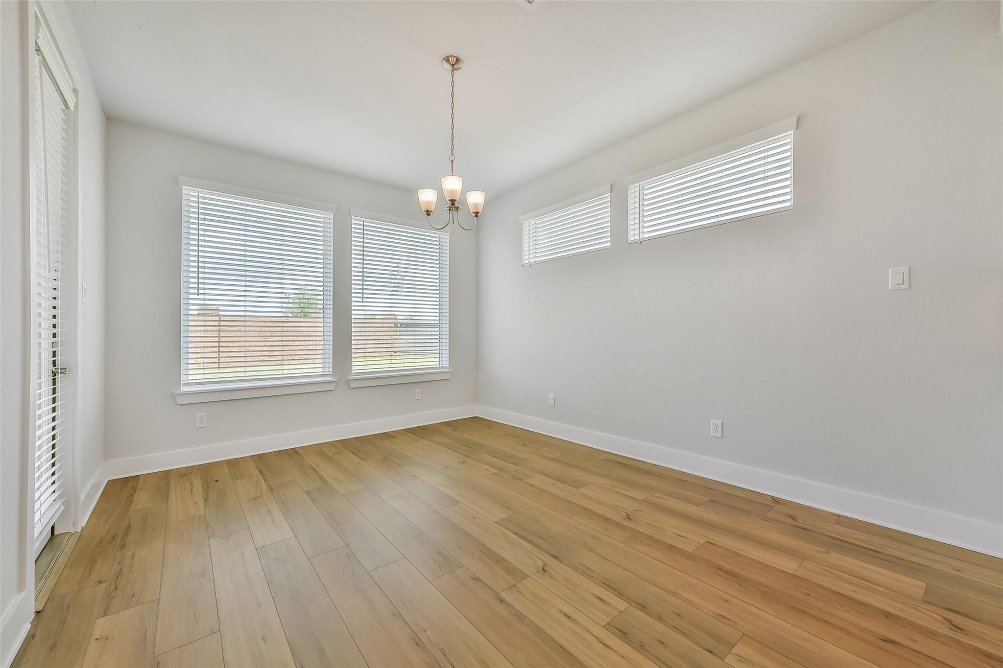 Bright empty dining room featuring oak hardwood floors, white blinds on clerestory windows, and modern chandelier in Davidson Homes The Victoria A, Lago Mar