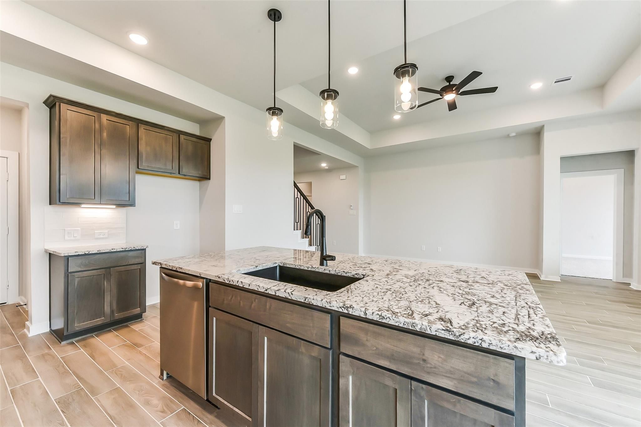 Modern kitchen island with quartz countertop, stainless dishwasher, and pendant lights in Davidson Homes Sequoia C, Crosby Texas