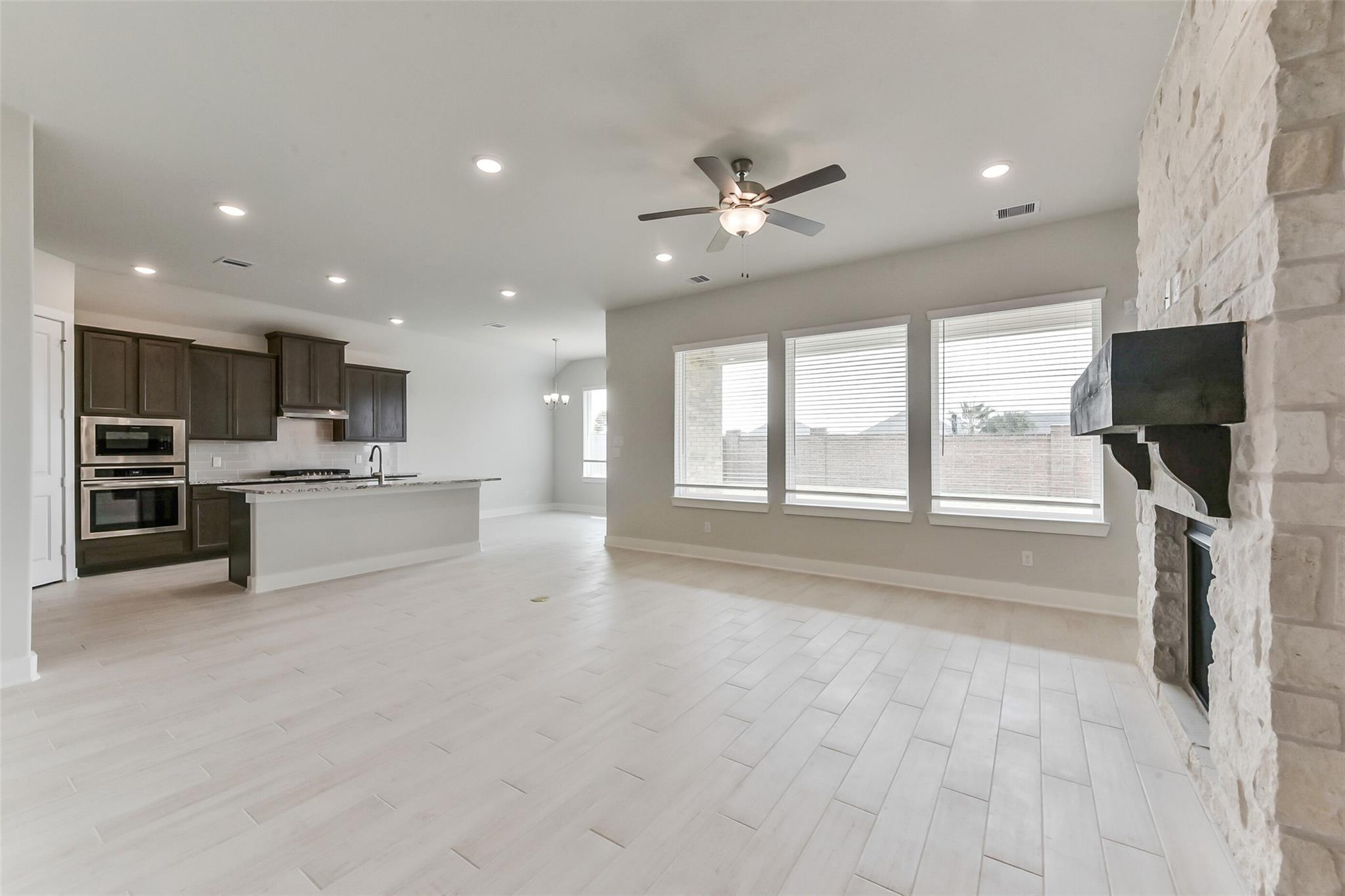 Open-concept living room and kitchen with stone fireplace in The Edward C floor plan by Davidson Homes in Lago Mar.