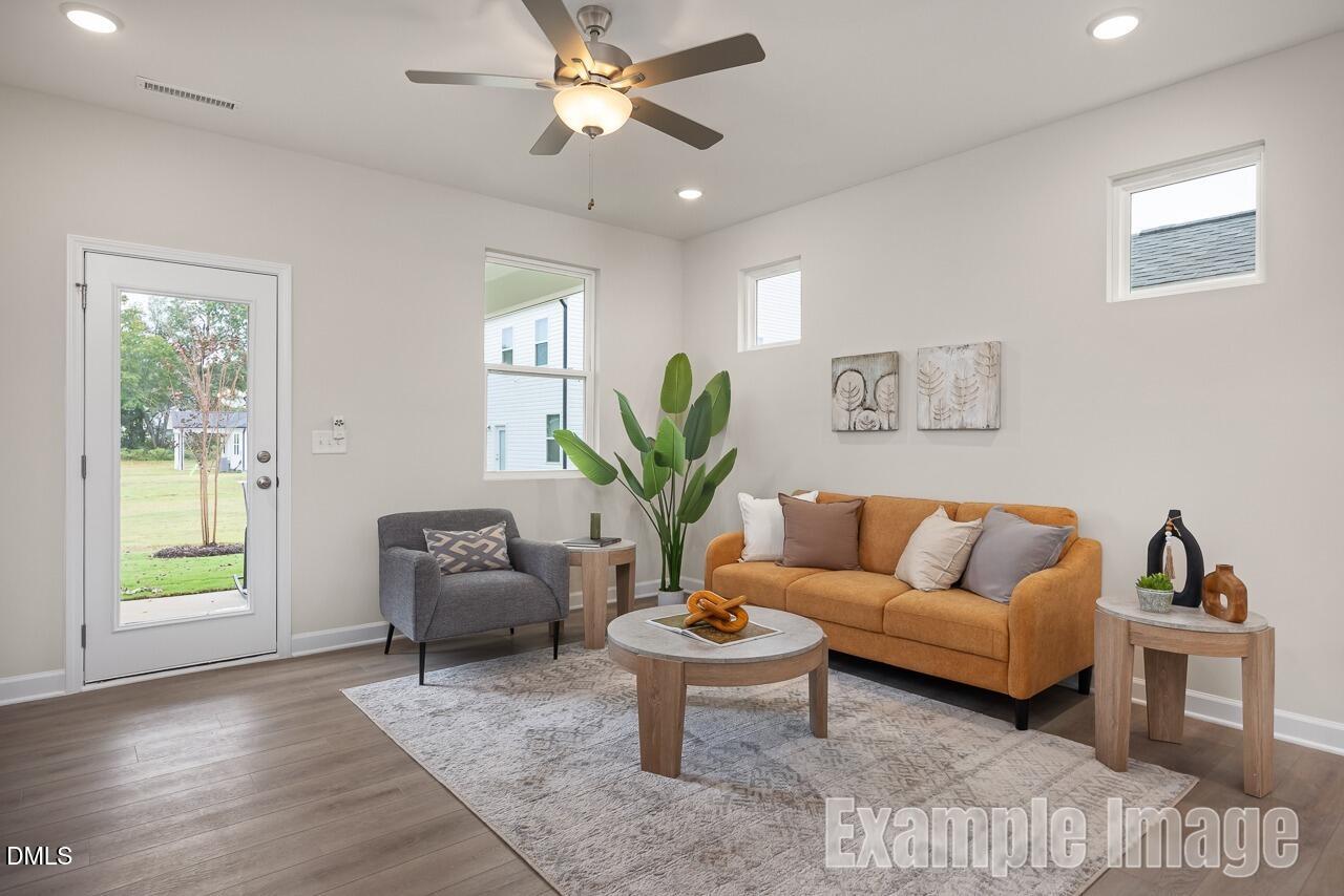 Cozy living room with orange sofa, gray armchair, potted plants, and sliding door to backyard in Davidson Homes The Carter C, Lillington, NC