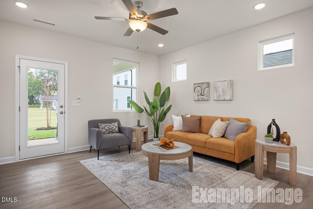 Cozy living room with orange sofa, gray armchair, potted plants, and sliding door to backyard in Davidson Homes The Carter C, Lillington, NC