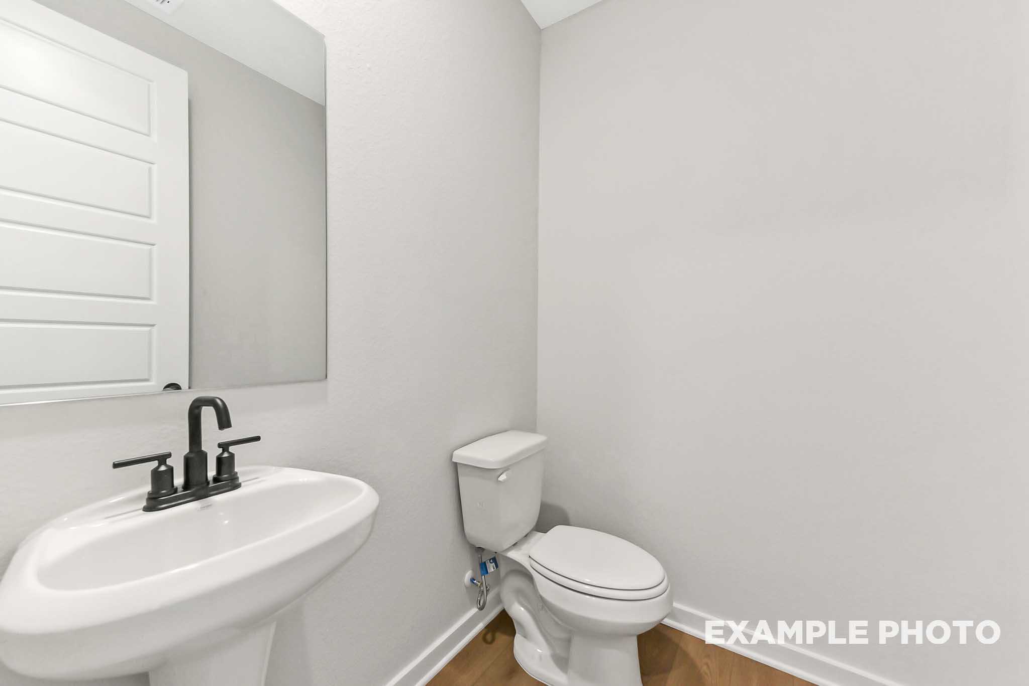 Powder room in The Sequoia home design featuring white pedestal sink, black faucet, toilet, and shiplap accents
