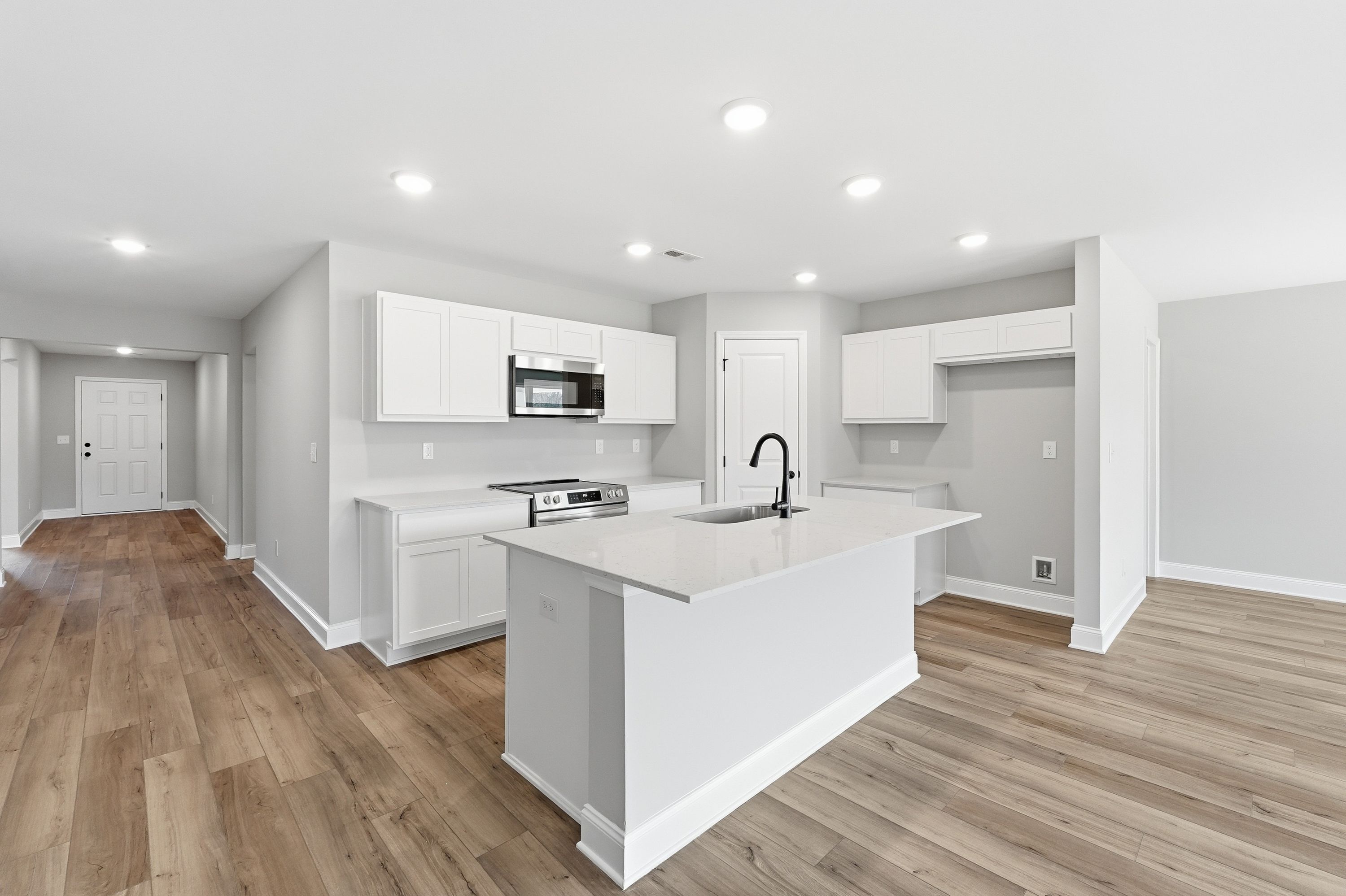 Spacious modern kitchen in The Daphne V by Davidson Homes featuring white shaker cabinets, quartz island with sink, stainless appliances, hardwood floors