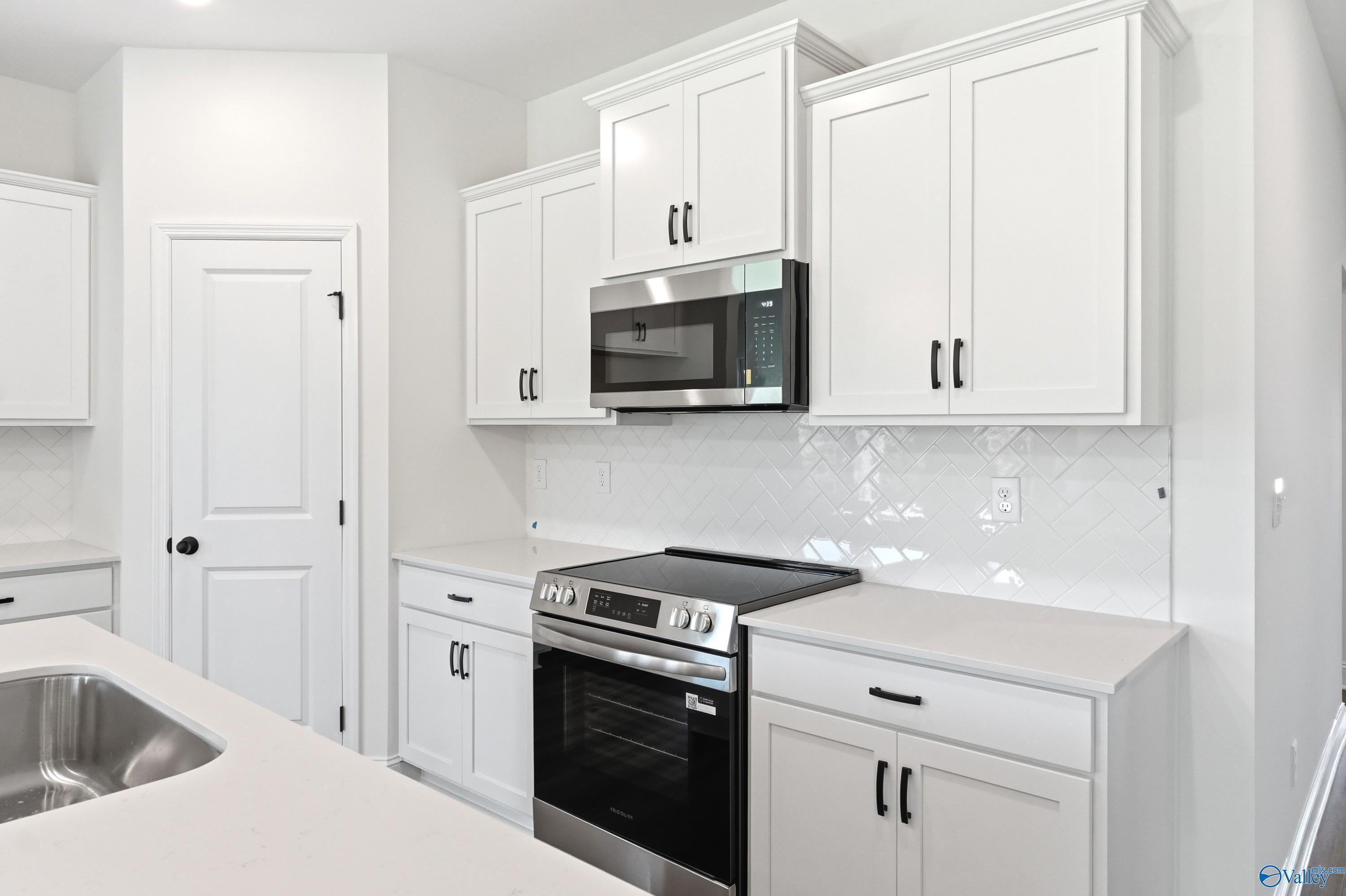 Modern kitchen with white cabinets, stainless steel appliances, and herringbone backsplash in The Daphne C, Ivy Hills, Toney.