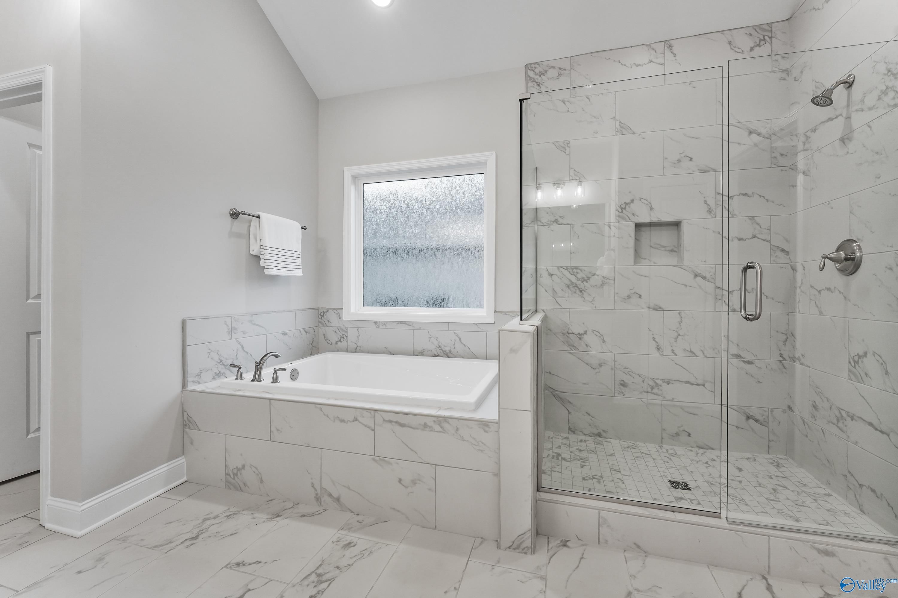Elegant master bathroom with freestanding tub, marble tile shower, and window in Davidson Homes The Finleigh, Toney, Alabama