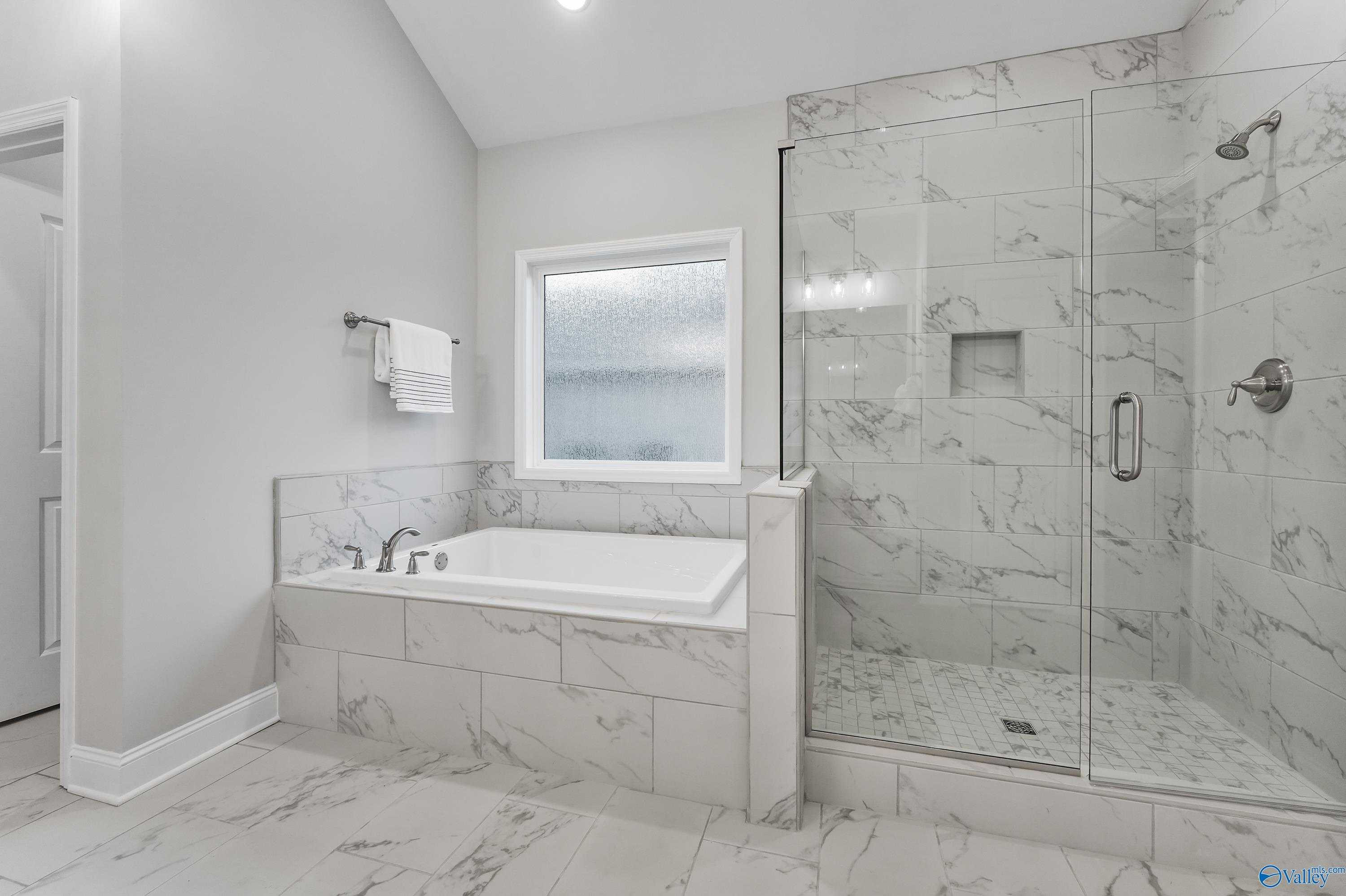 Elegant master bathroom featuring marble tiles, glass shower enclosure, freestanding tub in Davidson Homes The Finleigh, Toney, Alabama