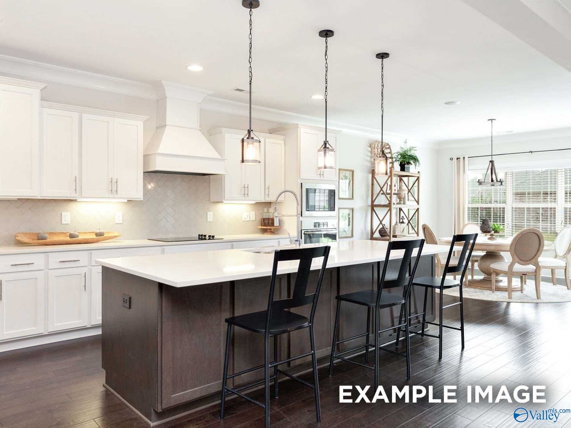 Modern open-concept kitchen with white cabinets, large island, black stools, and pendant lights in Davidson Homes The Finleigh, Meridianville, AL