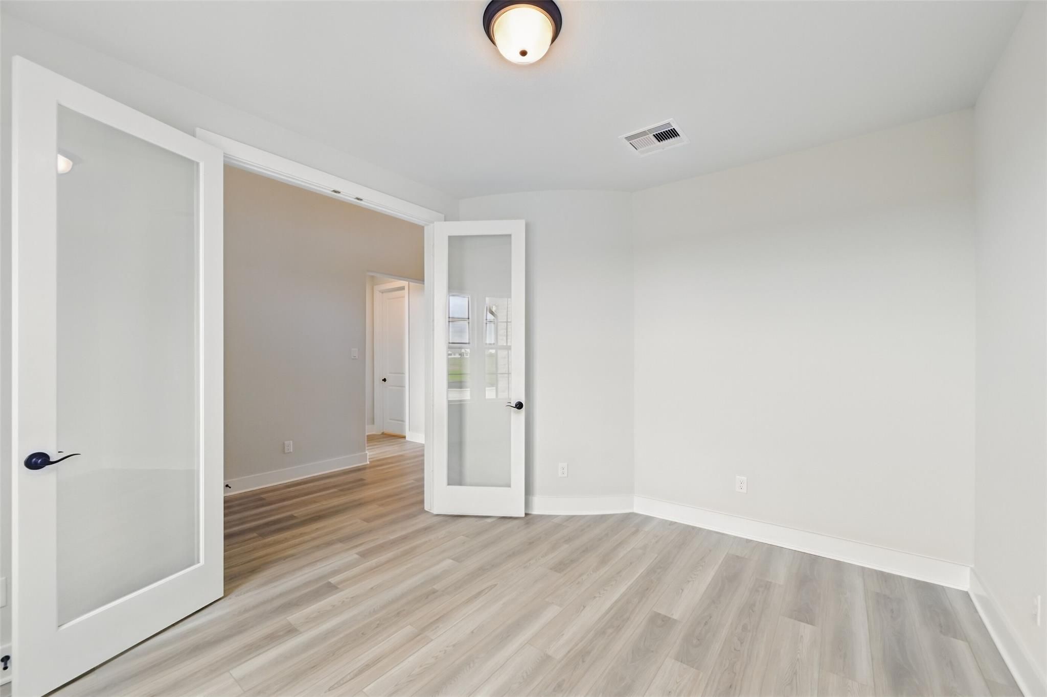 Bright corner study with open frosted glass French doors, light oak floors, white walls in Davidson Homes Victoria C, Lago Mar