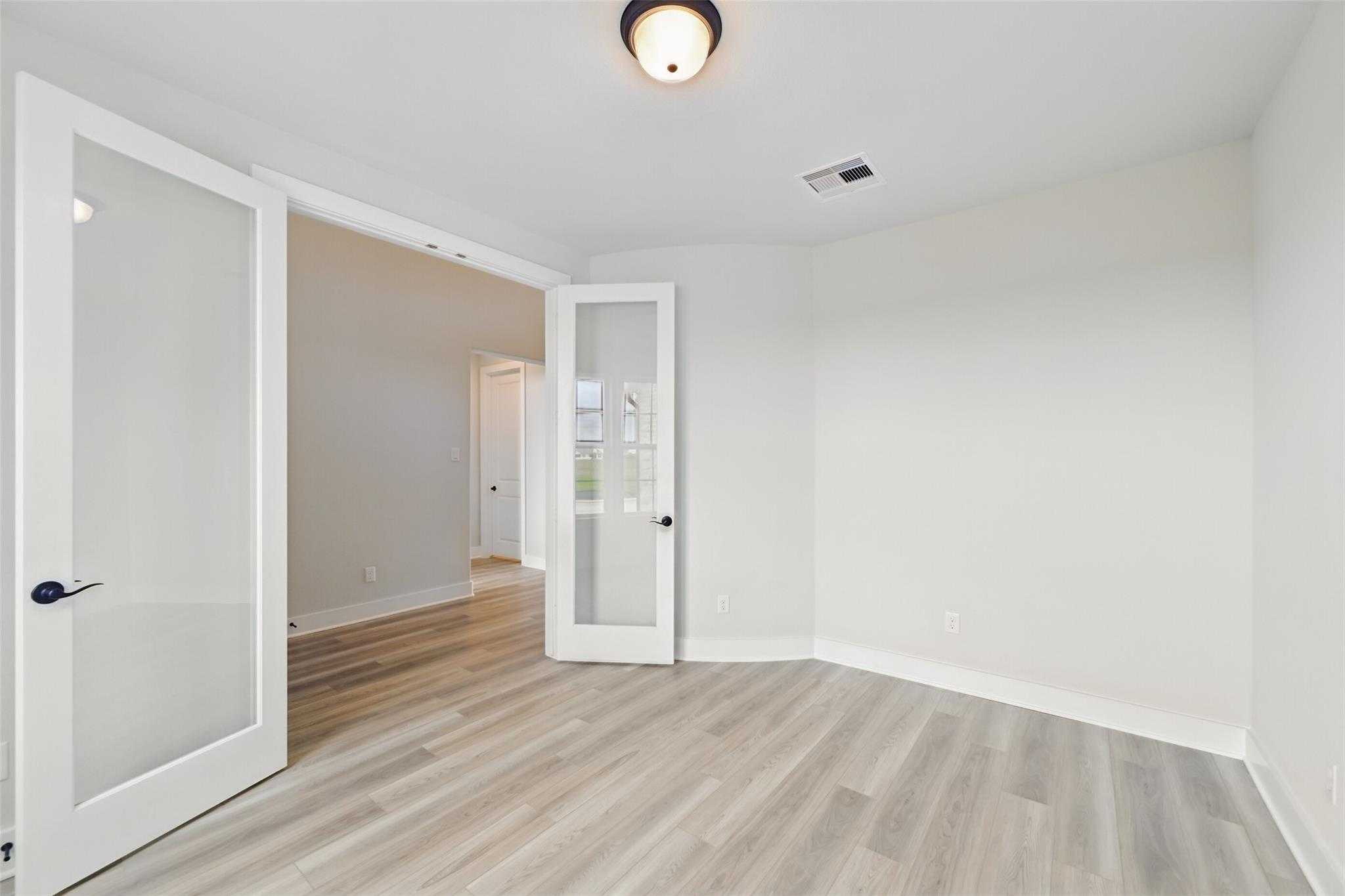 Bright flex room with open glass French doors, white walls, and light wood floors in Davidson Homes The Victoria C, Lago Mar, Texas City