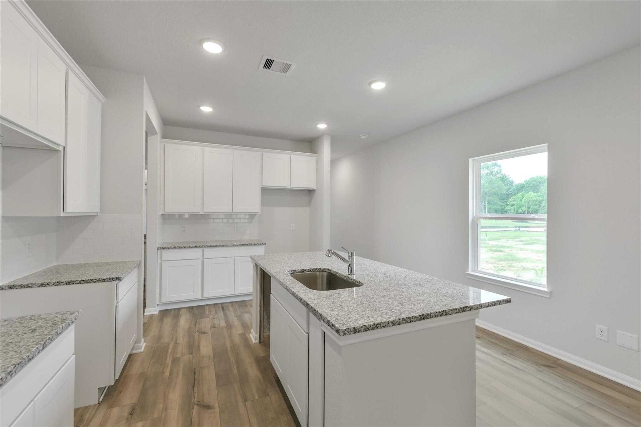 Modern kitchen featuring white cabinets, granite countertops, center island sink, and window view in The Frio G, Conroe, Texas