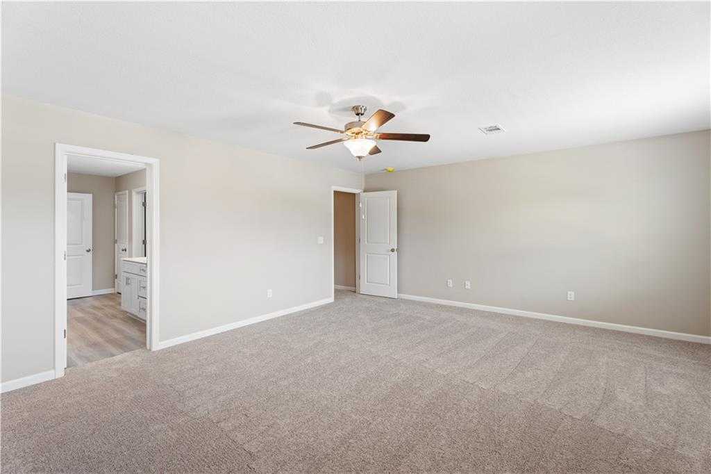 Spacious master bedroom with beige carpet, ceiling fan, and en-suite bath in Davidson Homes The Bartlett, Phenix City, AL