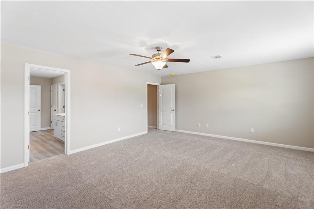 Spacious master bedroom with beige carpet, ceiling fan, and en-suite bath in Davidson Homes The Bartlett, Phenix City, AL