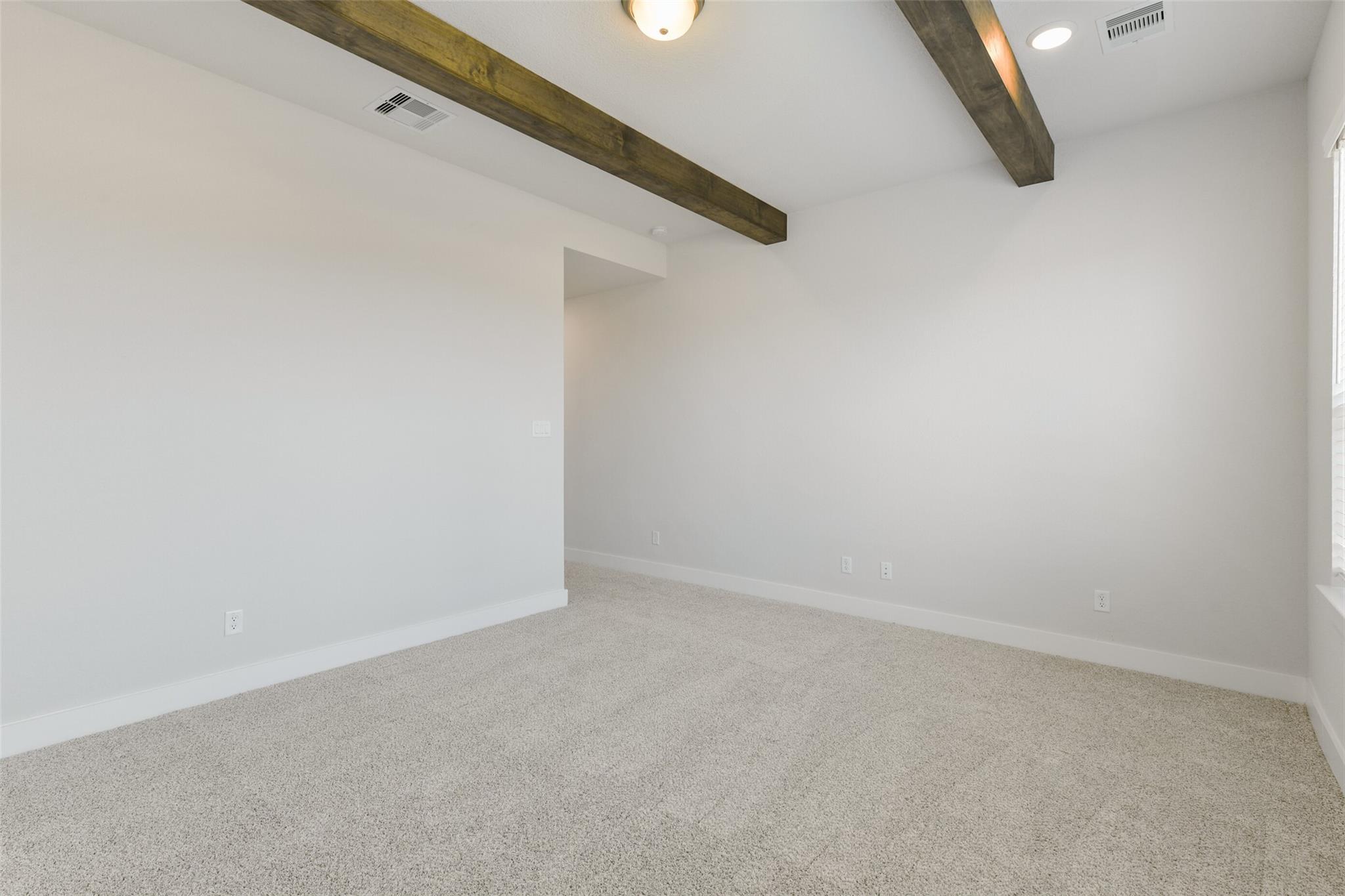 Spacious living room with exposed wooden beam ceiling, white walls, and beige carpet in Davidson Homes Edward A, Lago Mar