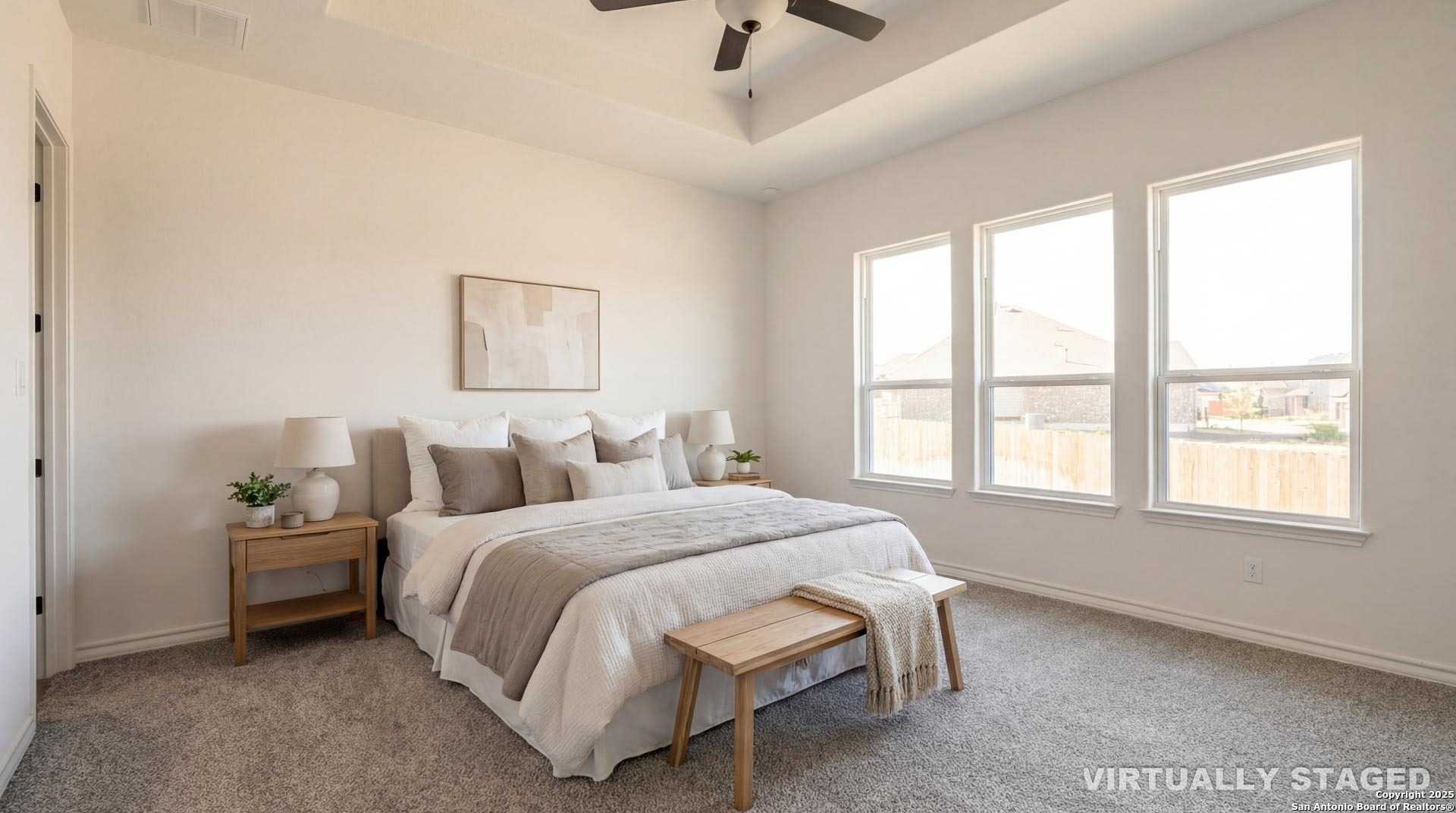 Luxurious master bedroom with tray ceiling, neutral bedding, and large windows in Davidson Homes The Garner B, Castroville, Texas